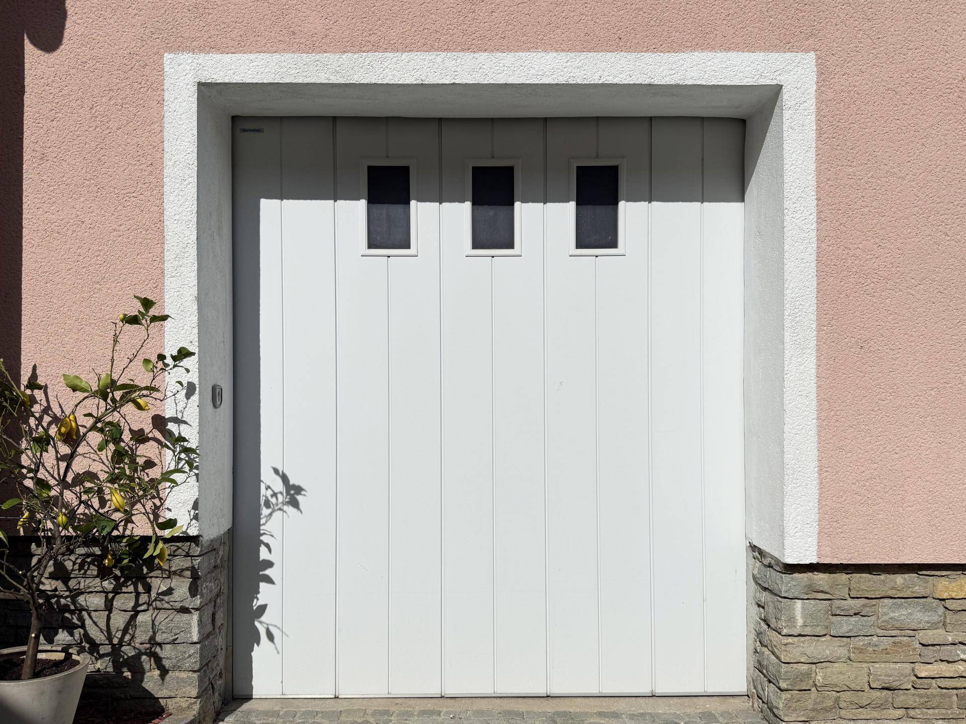 Weißes Garagentor mit drei kleinen Fenstern, umgeben von einer hellen Fassade.