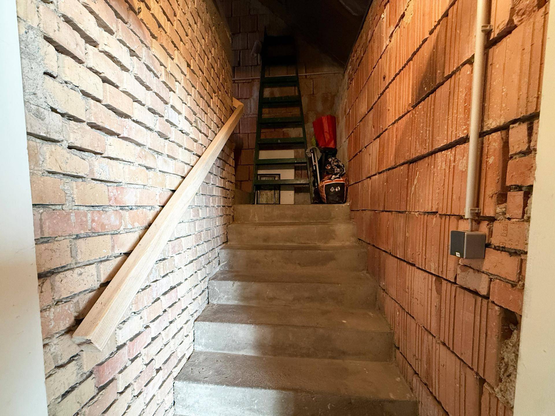 Unfertiger Kellerraum mit Ziegelwänden und einer Betontreppe.
