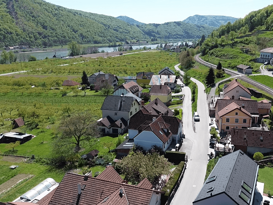 Luftaufnahme eines Dorfes mit Häusern, Feldern und einem Fluss im Hintergrund.