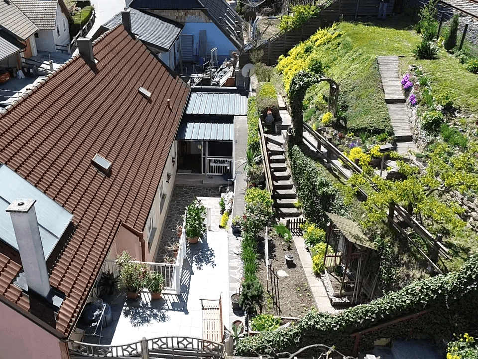 Luftaufnahme des Hauses mit Ziegeldach und dem terrassierten Gartenbereich.