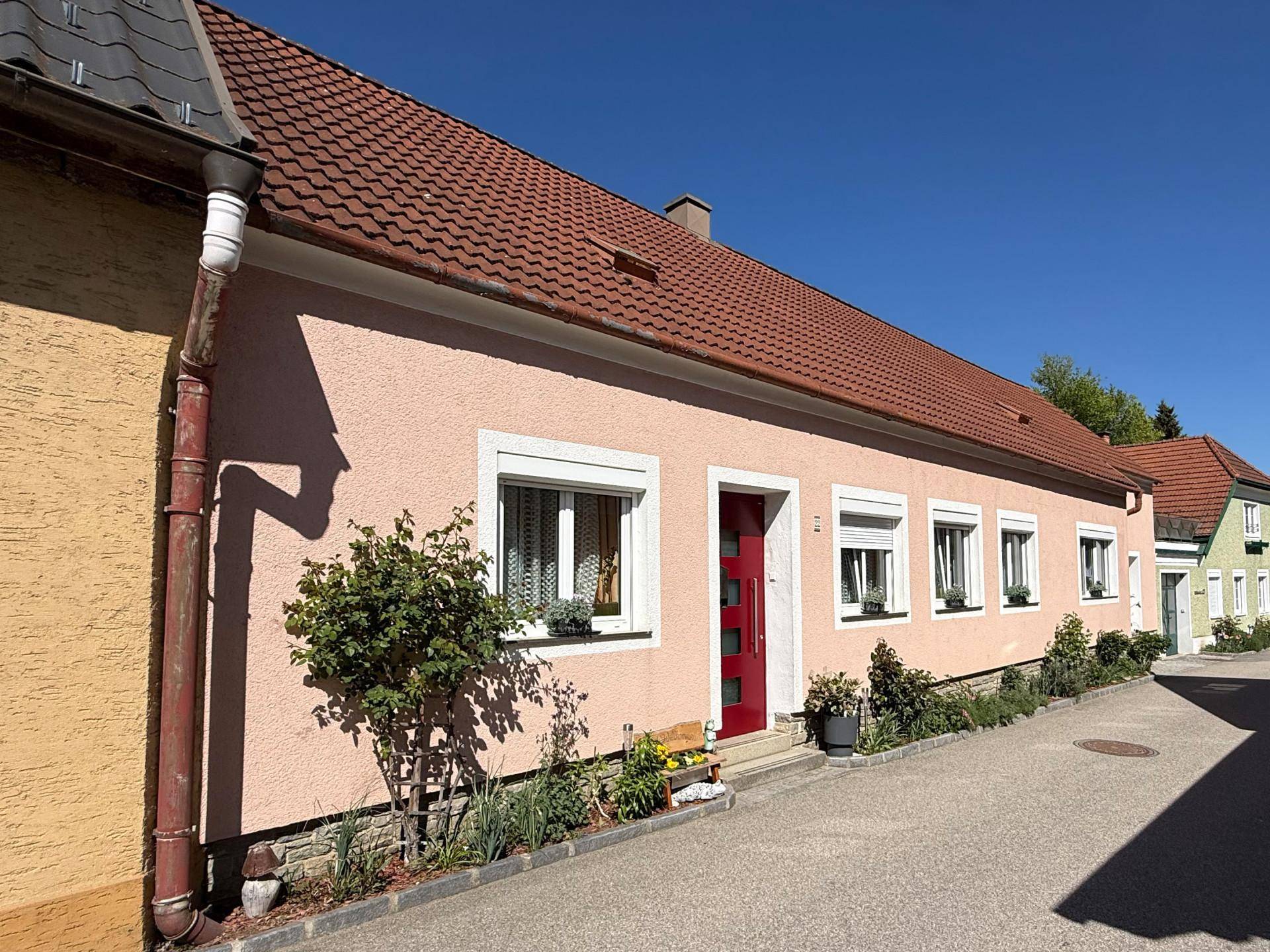 Ansicht des Hauses von der Straße mit rosafarbener Fassade und gepflegtem Vorgarten.