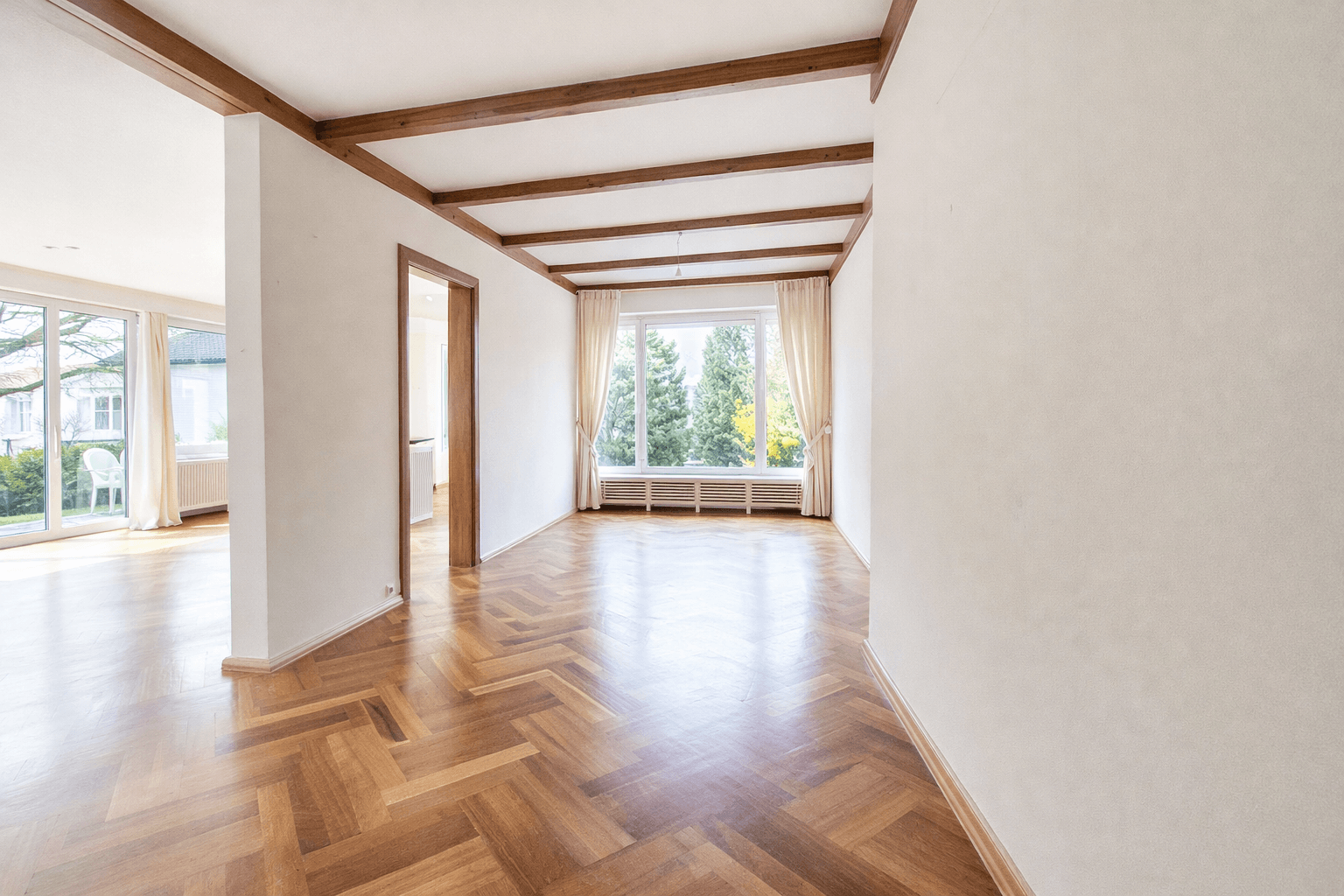 Heller Wohnbereich mit Holzbalkendecke und Fischgrätparkett, verbunden mit dem Hauptwohnzimmer.