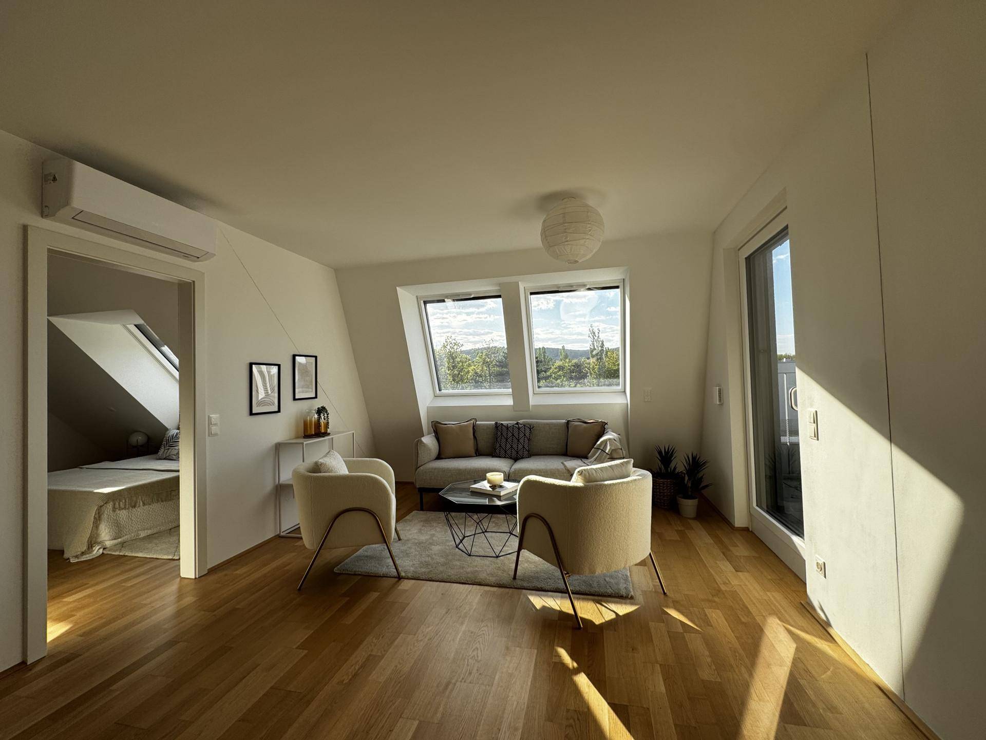 Lichtdurchflutetes Wohnzimmer mit Holzboden und Zugang zu einem weiteren Schlafzimmer.
