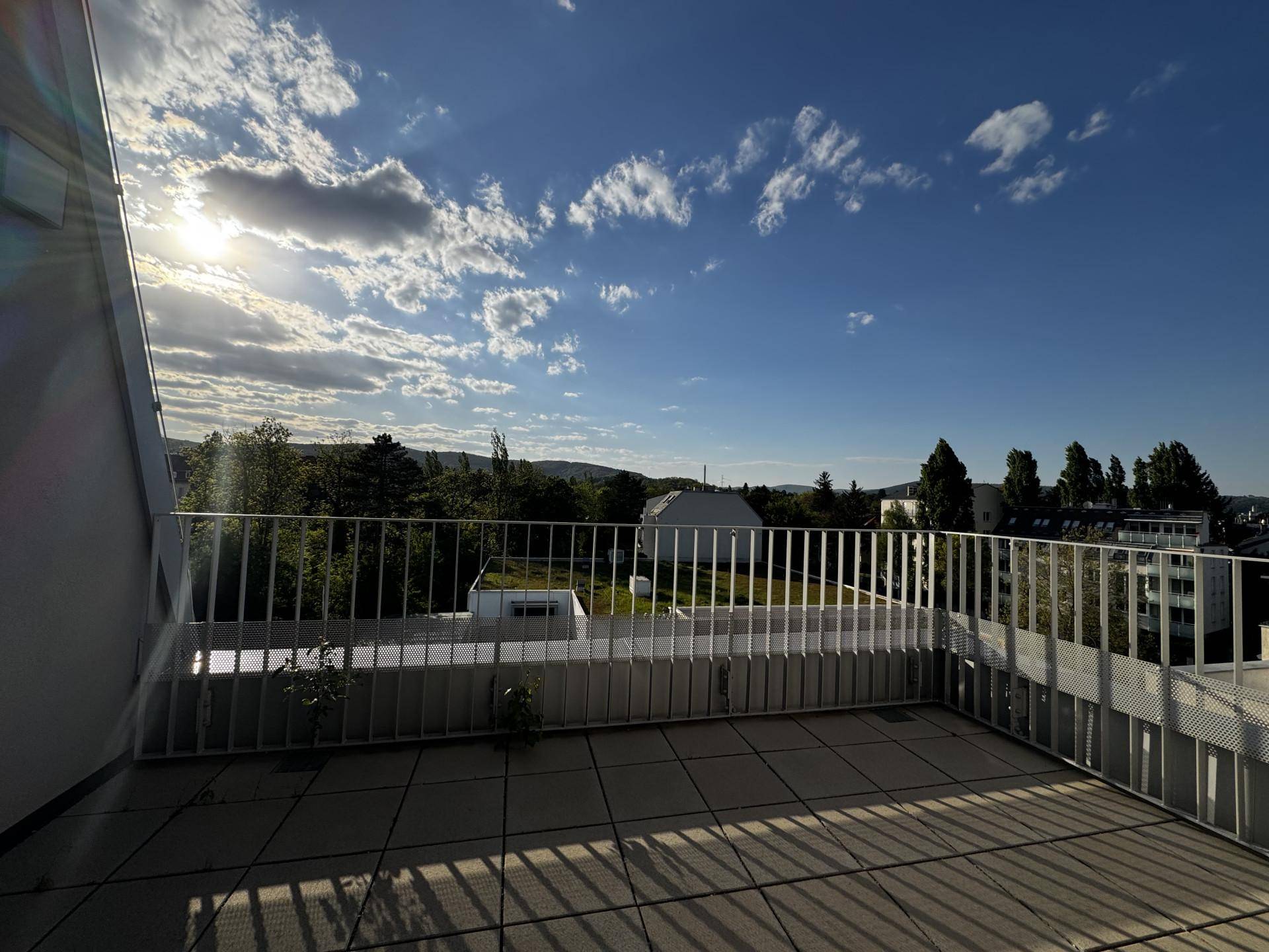Sonniger Balkon mit Fliesenboden und Panoramablick auf die grüne Umgebung und den Himmel.