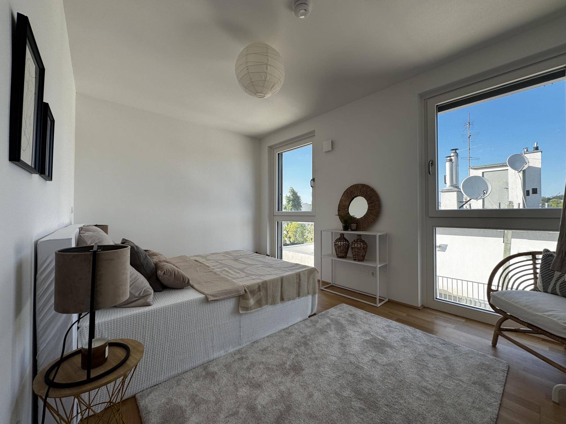 Schlafzimmer mit Holzboden, großen Fenstern und Blick auf die umliegenden Gebäude.