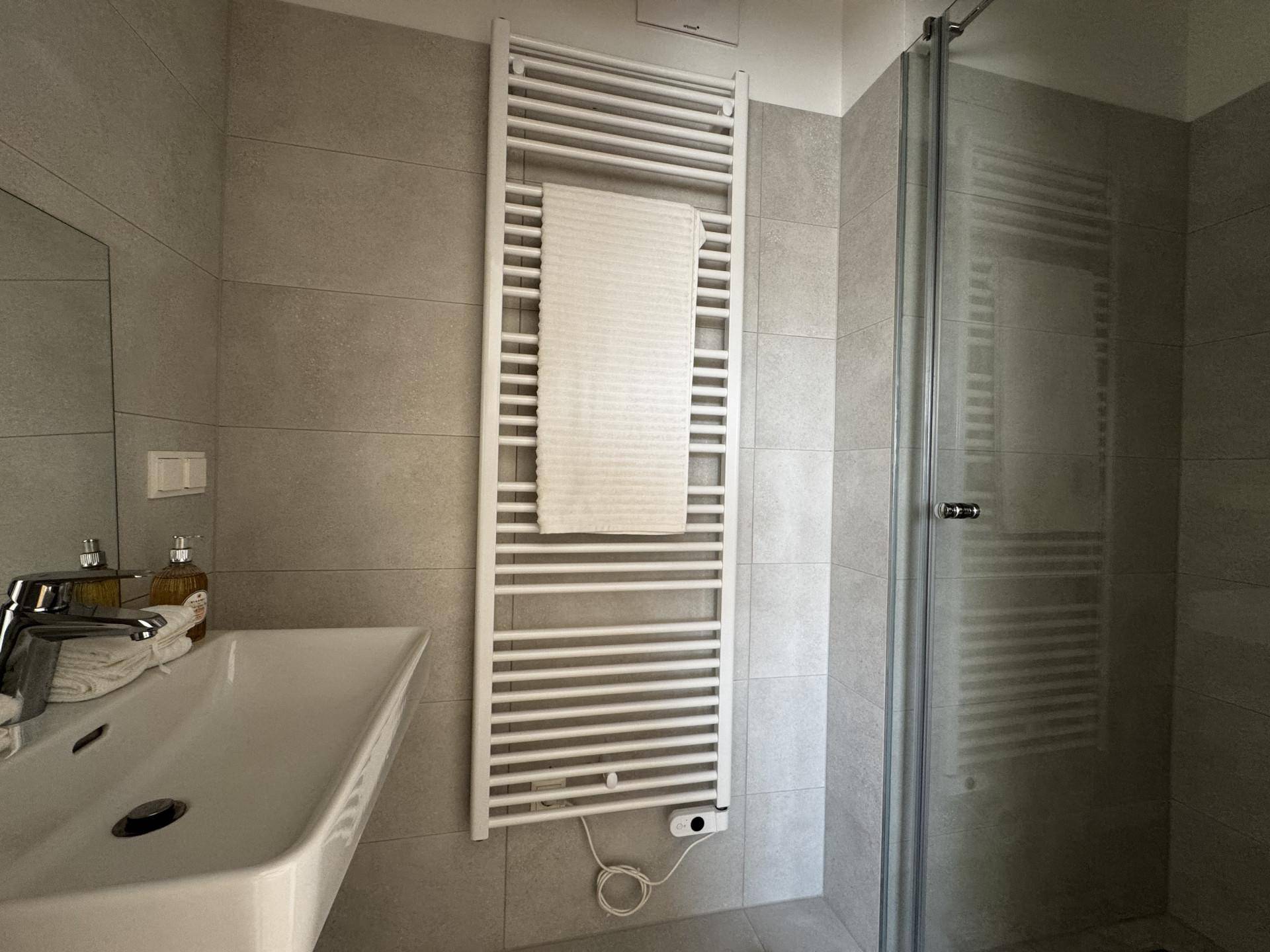 Modernes Badezimmer mit grauen Fliesen, Dusche und beheiztem Handtuchhalter.