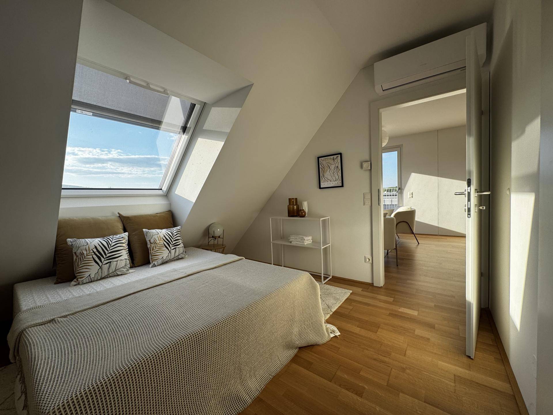 Gemütliches Schlafzimmer mit Holzboden, Dachfenster und Blick in den Wohnbereich.