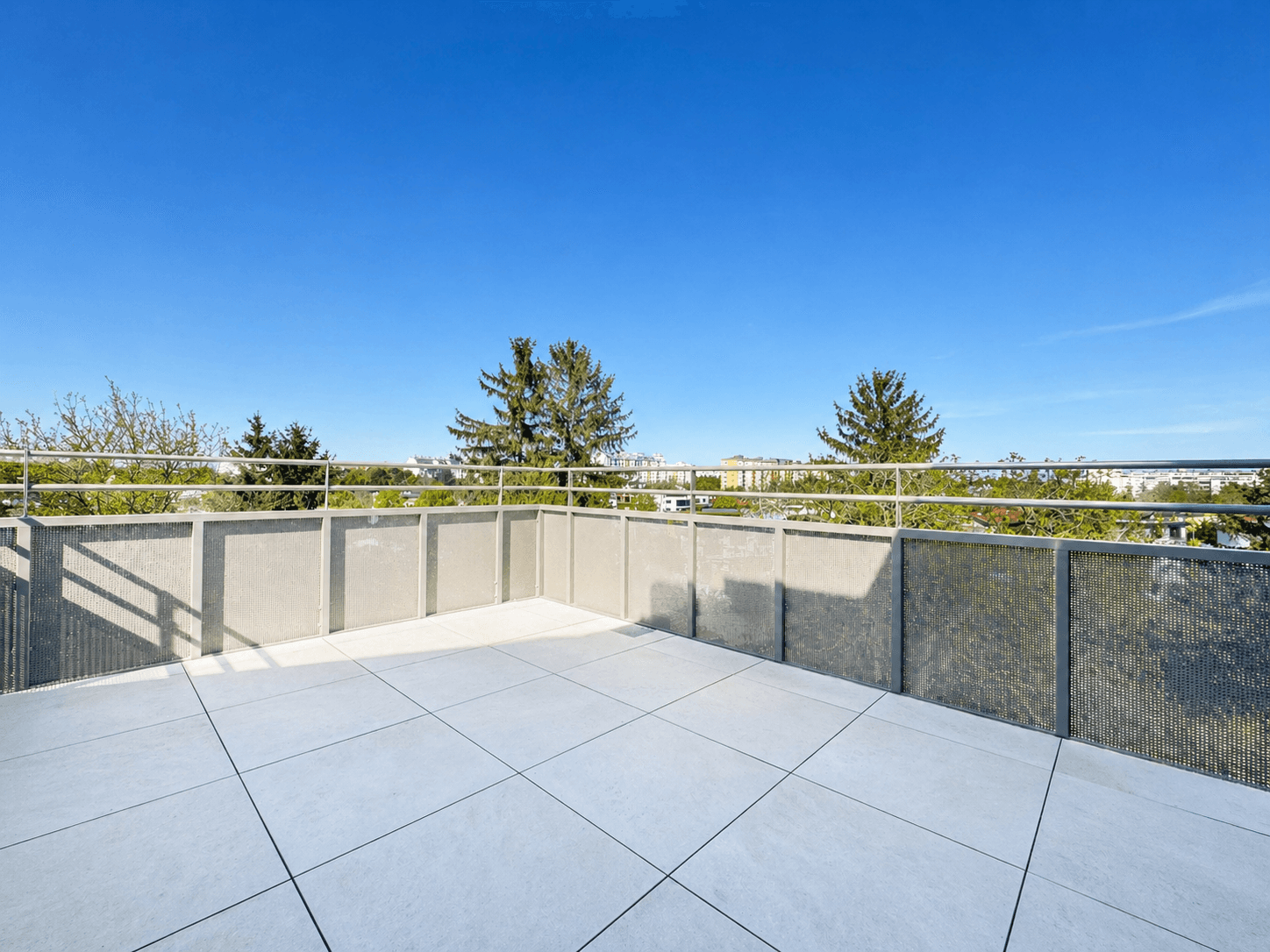 Große geflieste Terrasse mit Metallgeländer und weitem Blick ins Grüne und auf die Stadt.