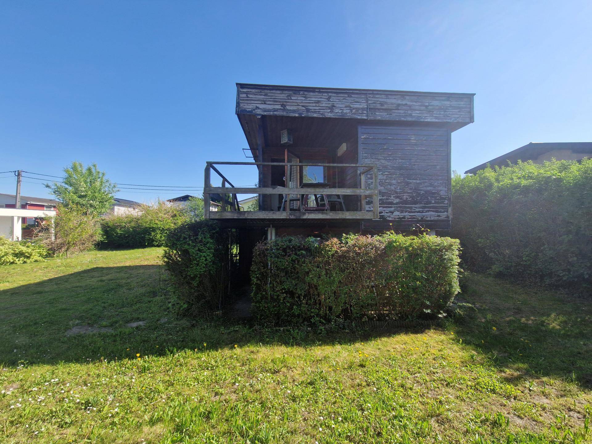 Seitenansicht des Holzhauses mit kleinem Balkon und einer gepflegten Hecke im Vordergrund.