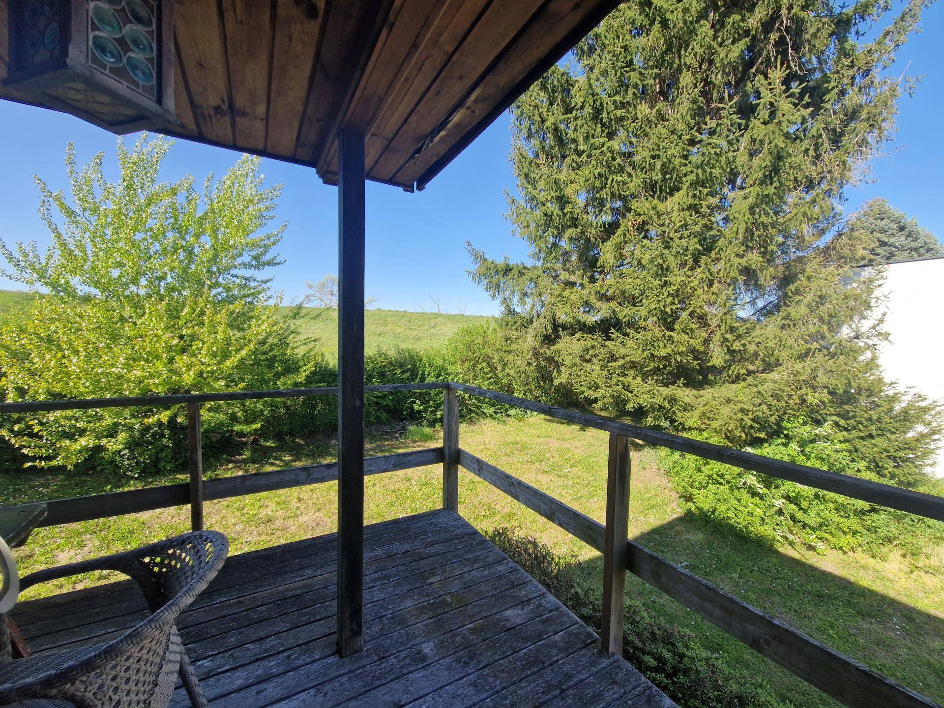 Gemütlicher Balkon mit Korbstuhl und weitem Blick ins Grüne unter strahlend blauem Himmel.