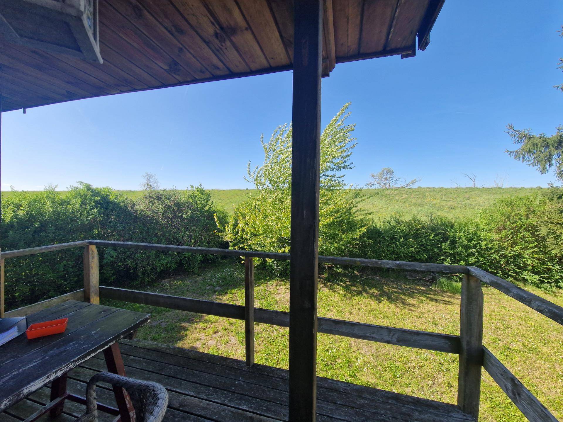 Balkon mit Holztisch und weitem Ausblick auf die umliegende Natur und grüne Hügel.