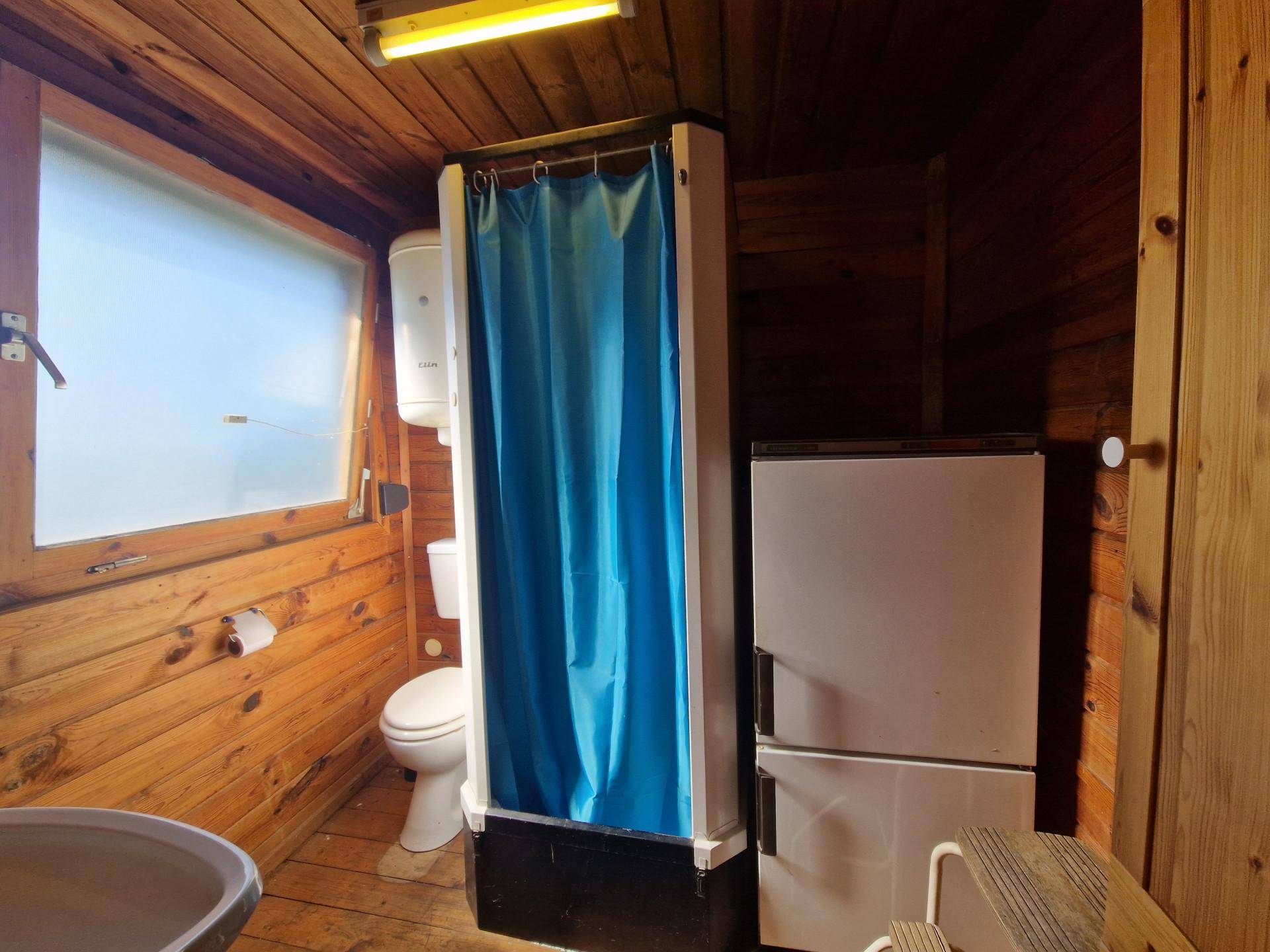 Kleines Badezimmer mit Holzvertäfelung, Dusche, Toilette und Fenster für Tageslicht.
