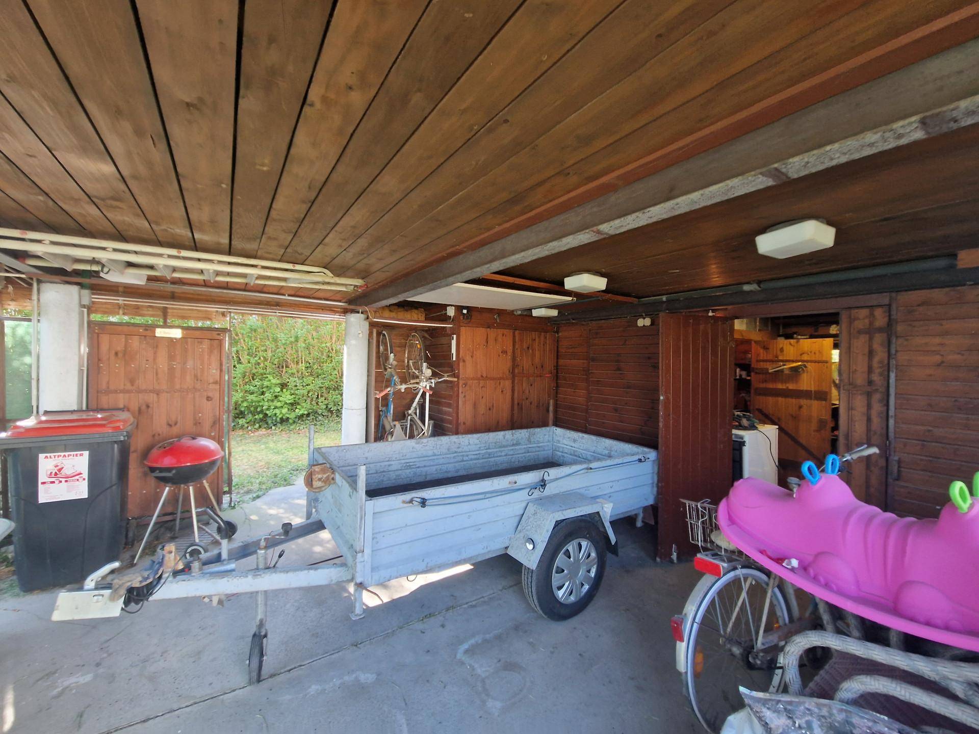 Überdachter Außenbereich mit Betonboden, Anhänger, Grill und Stauraum.