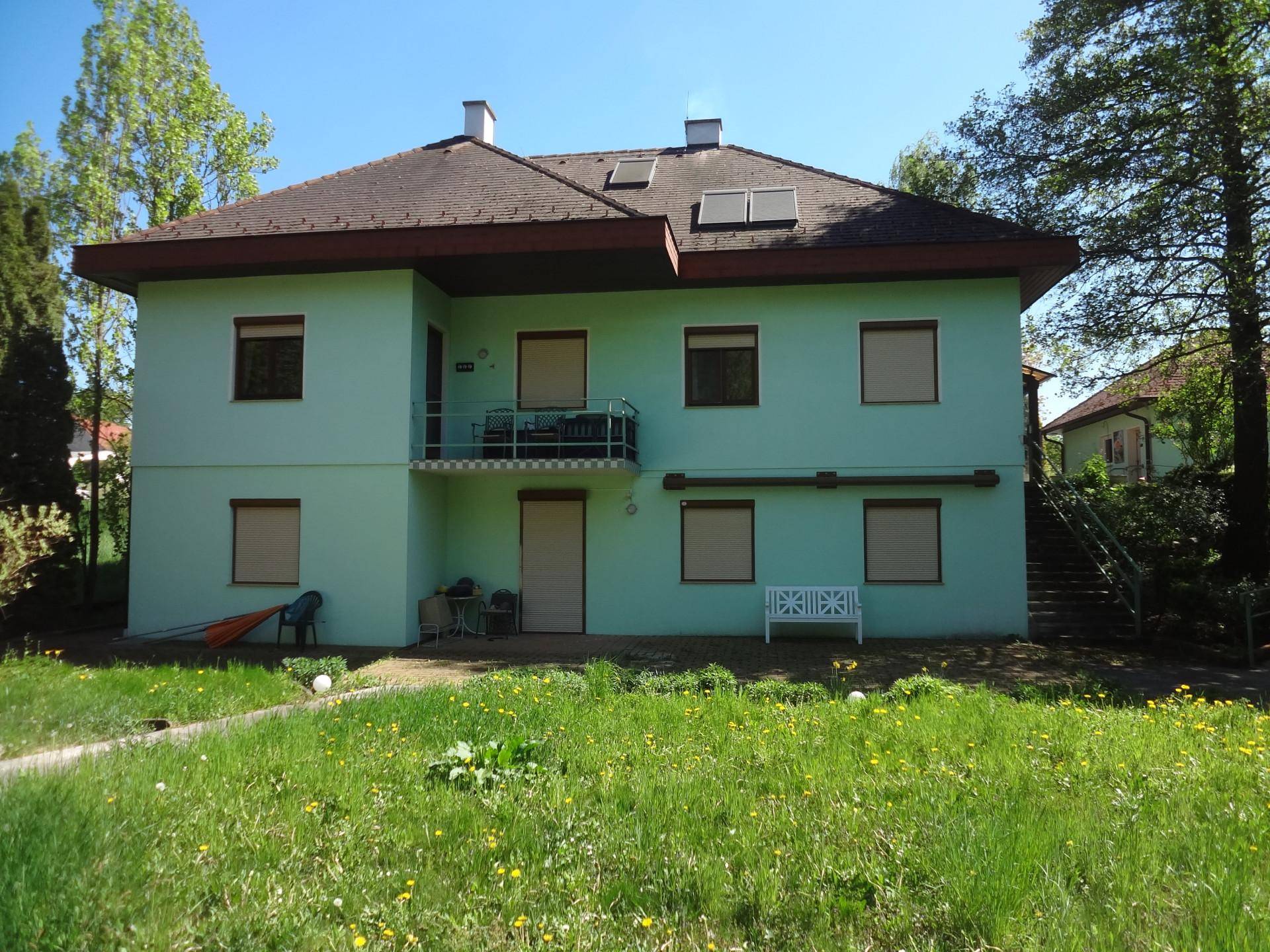 Rückseite des Hauses mit einem kleinen Balkon und Blick auf die weitläufige Rasenfläche.