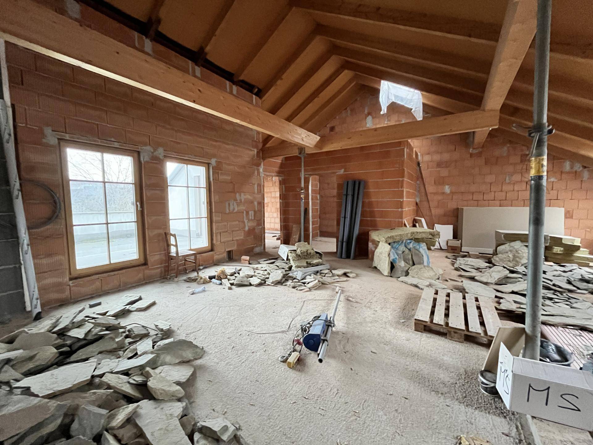 Großer Raum im Rohbau mit Holzbalken, Ziegelwänden und Baumaterialien.