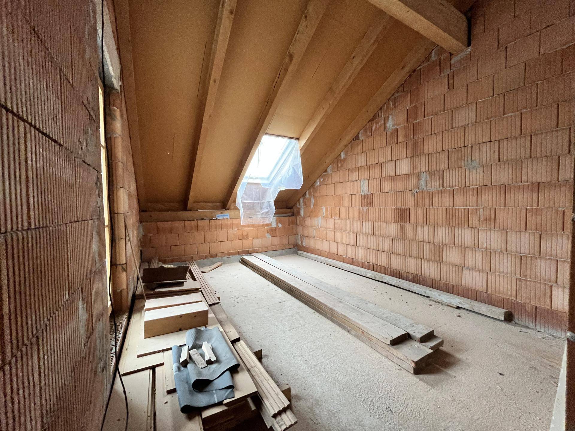 Dachgeschoss im Rohbau mit Holzbalken, Dachfenster und Ziegelwänden.