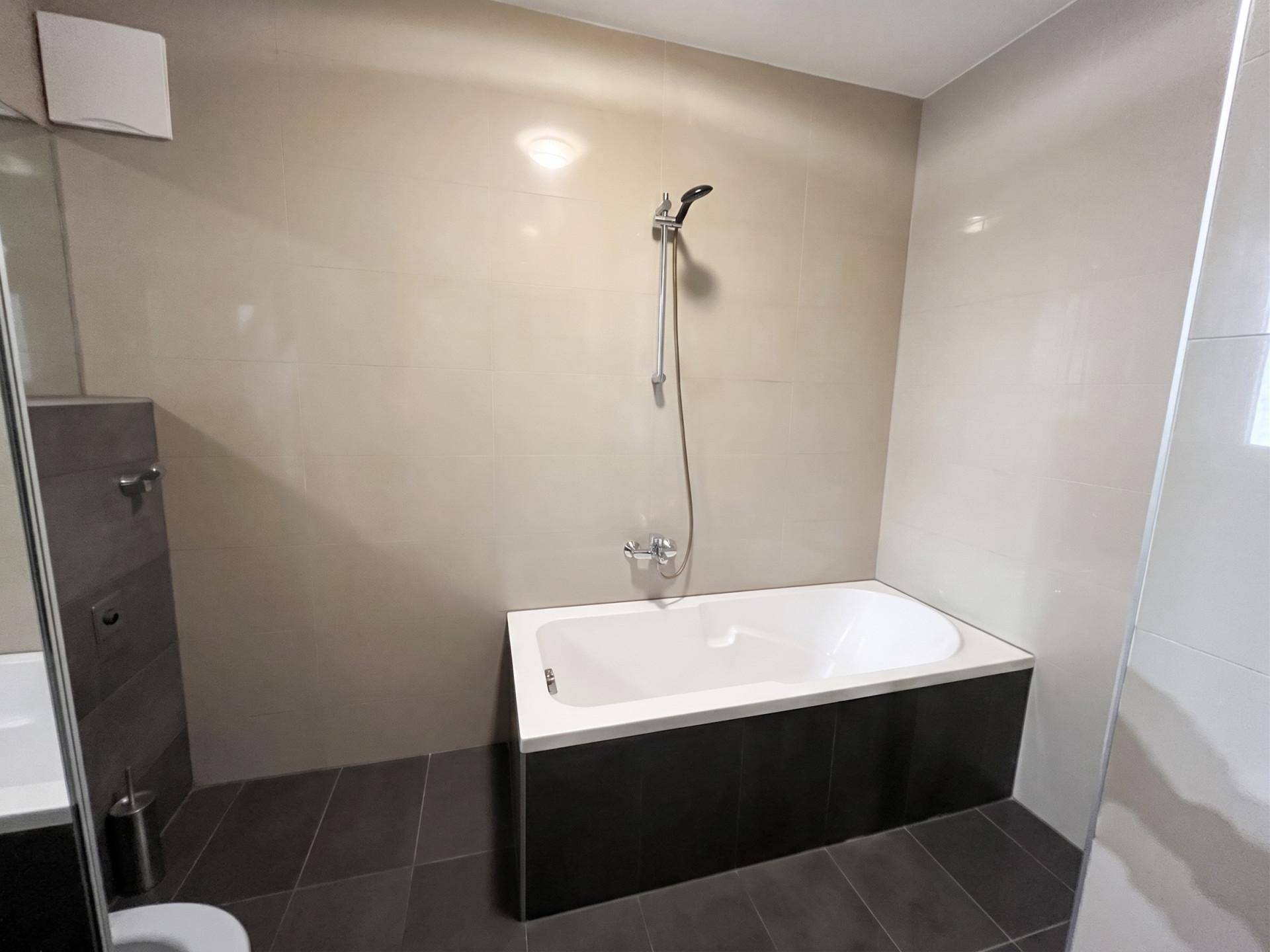 Modernes Badezimmer mit Badewanne, grauen Fliesen und minimalistischem Design.