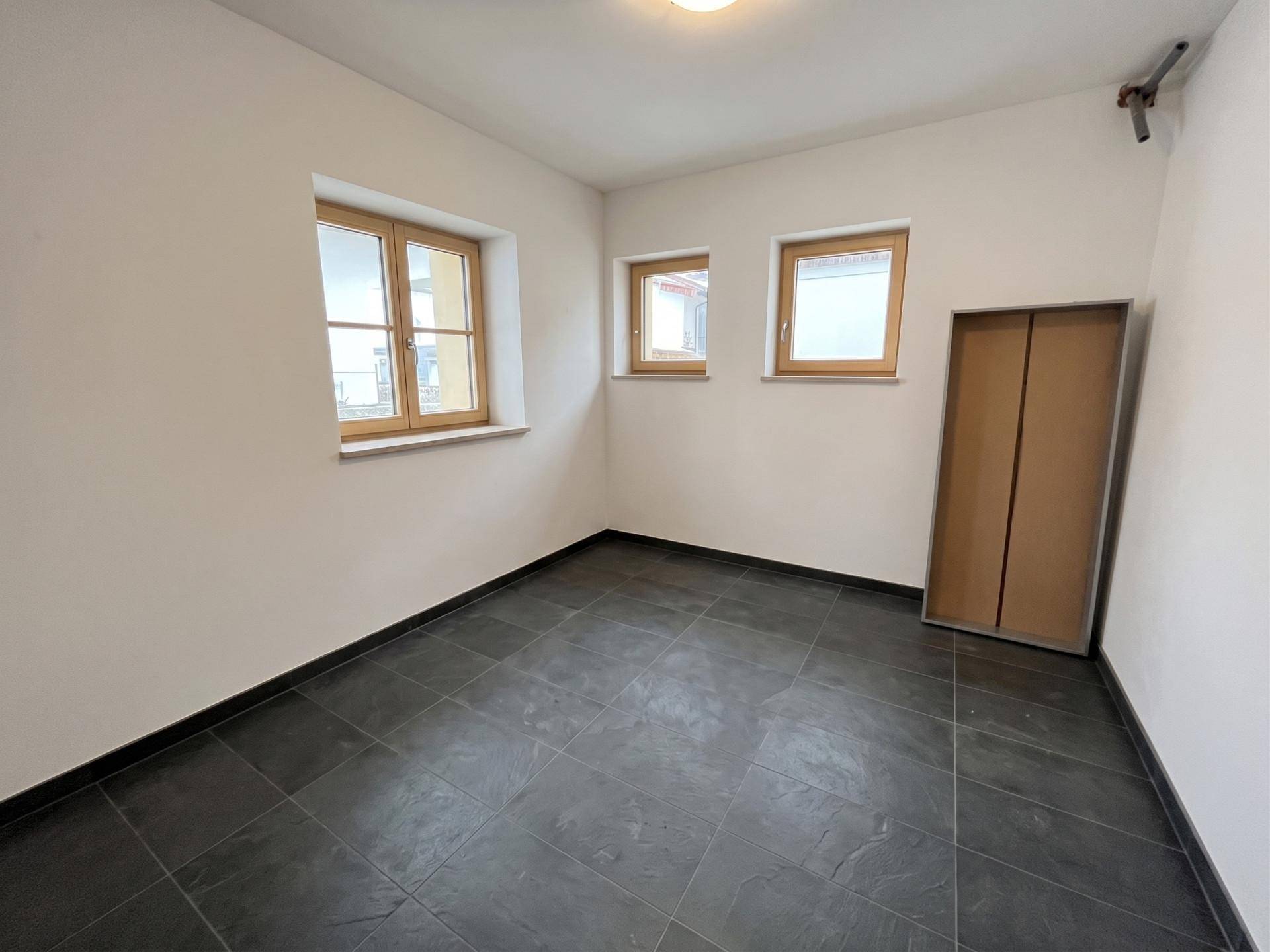 Kleiner Raum mit dunklen Fliesen und drei Fenstern, ideal als Kinderzimmer oder Büro.