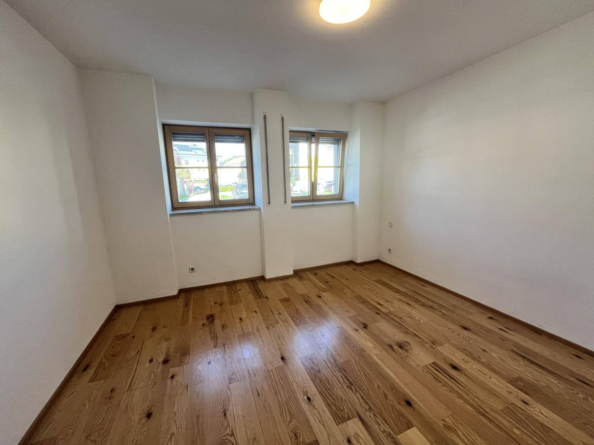Leeres Zimmer mit Holzfußboden und zwei Fenstern, ideal als Schlaf- oder Arbeitszimmer.