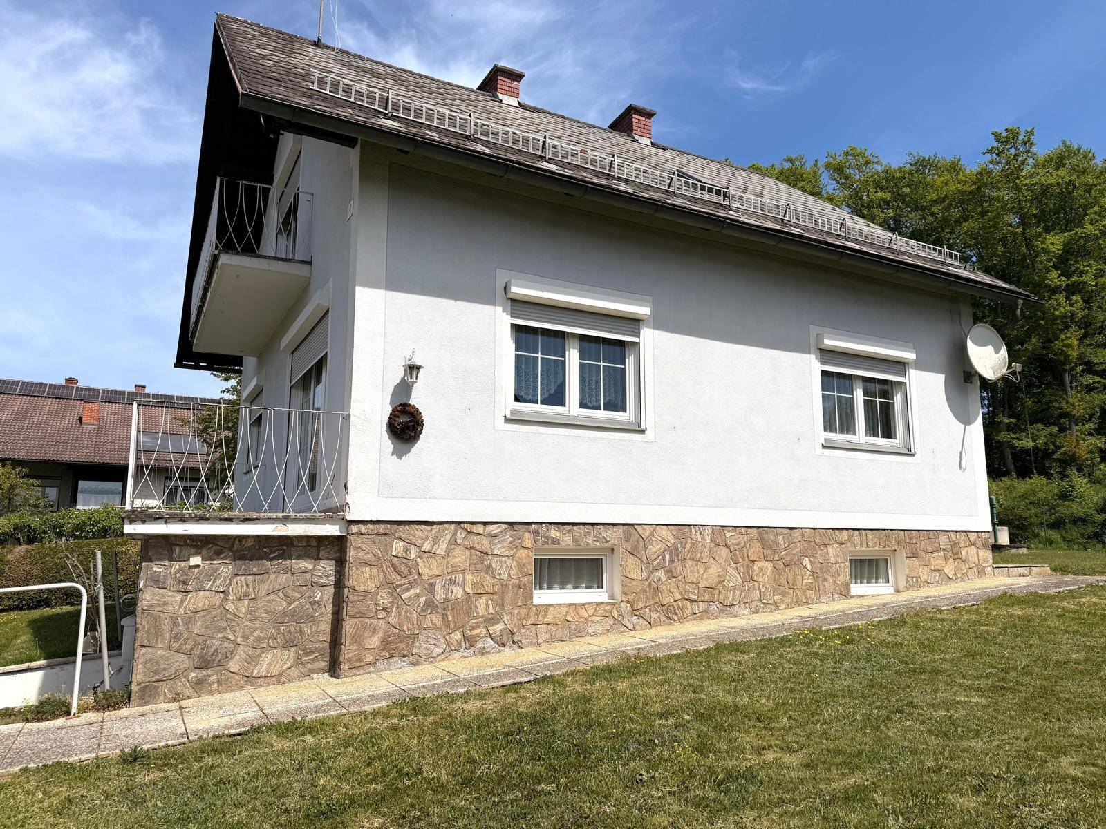 Seitenansicht des Hauses mit Steinsockel, Balkonen und Rollläden.