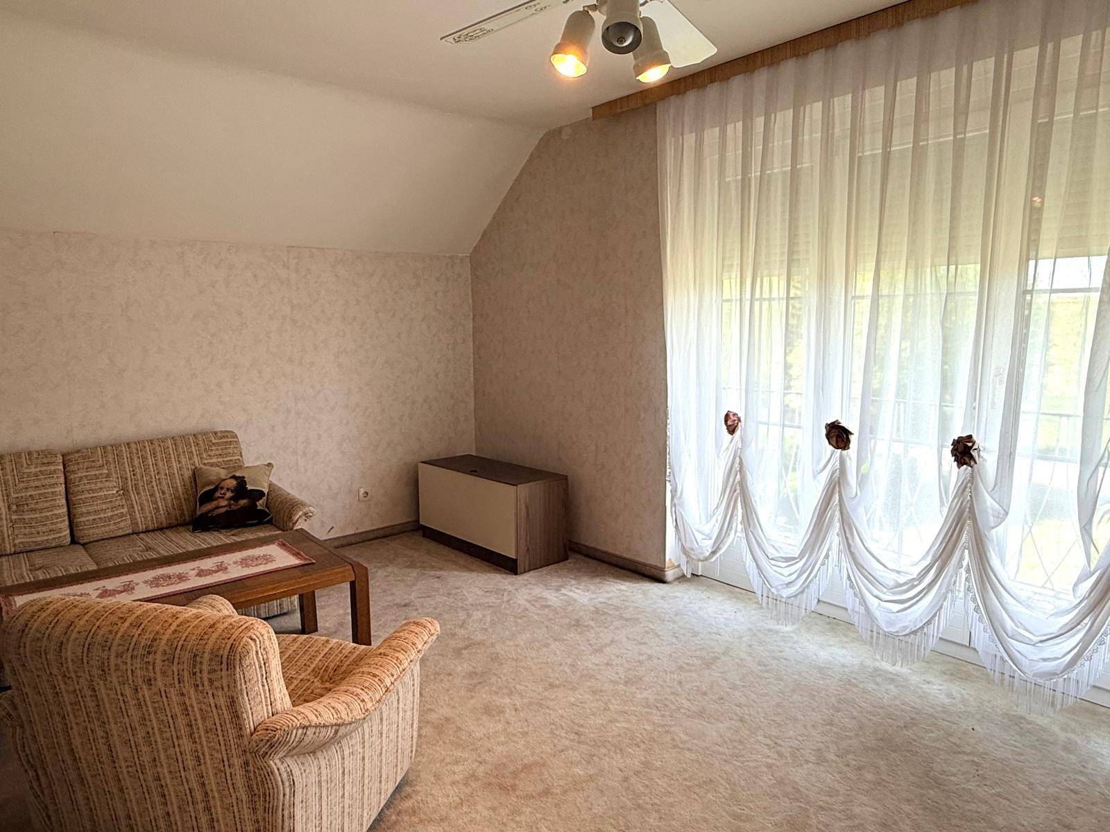 Wohnzimmer im Dachgeschoss mit Sofa, Sessel und Teppichboden.