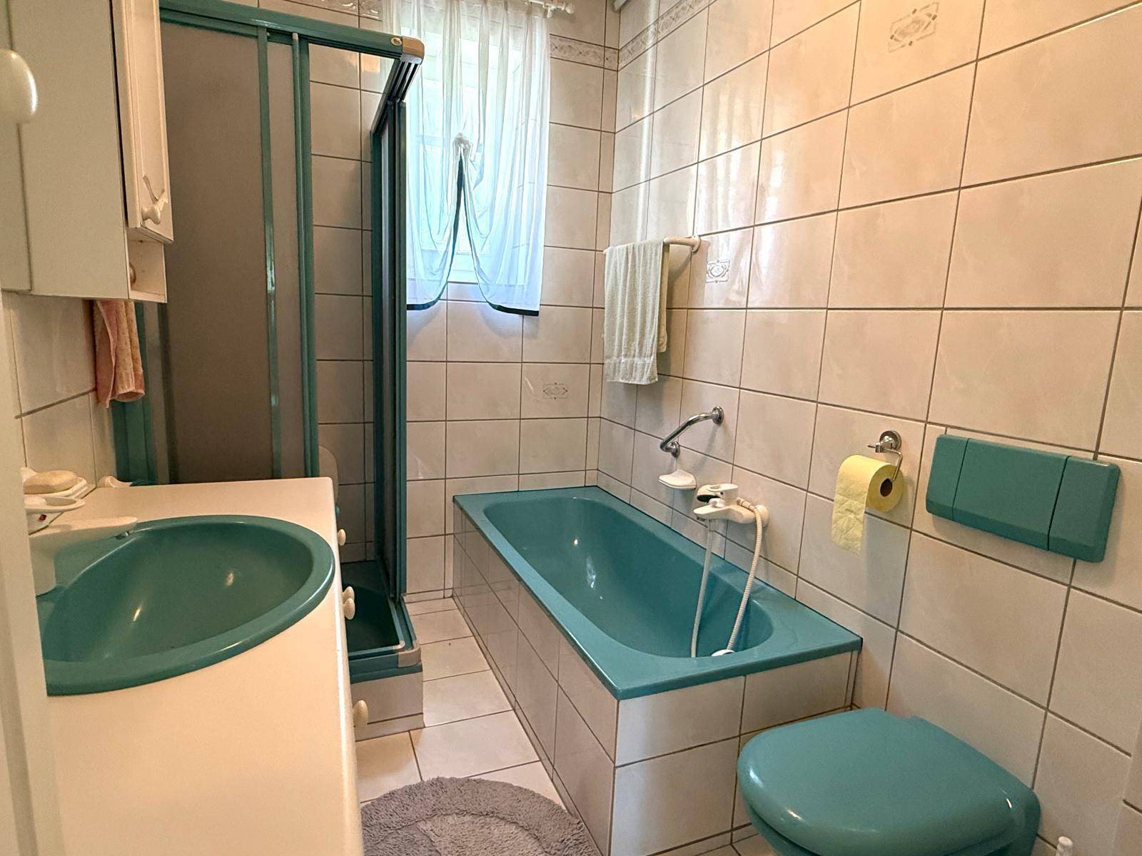 Badezimmer mit türkisfarbener Badewanne, Waschbecken und hell gefliesten Wänden.