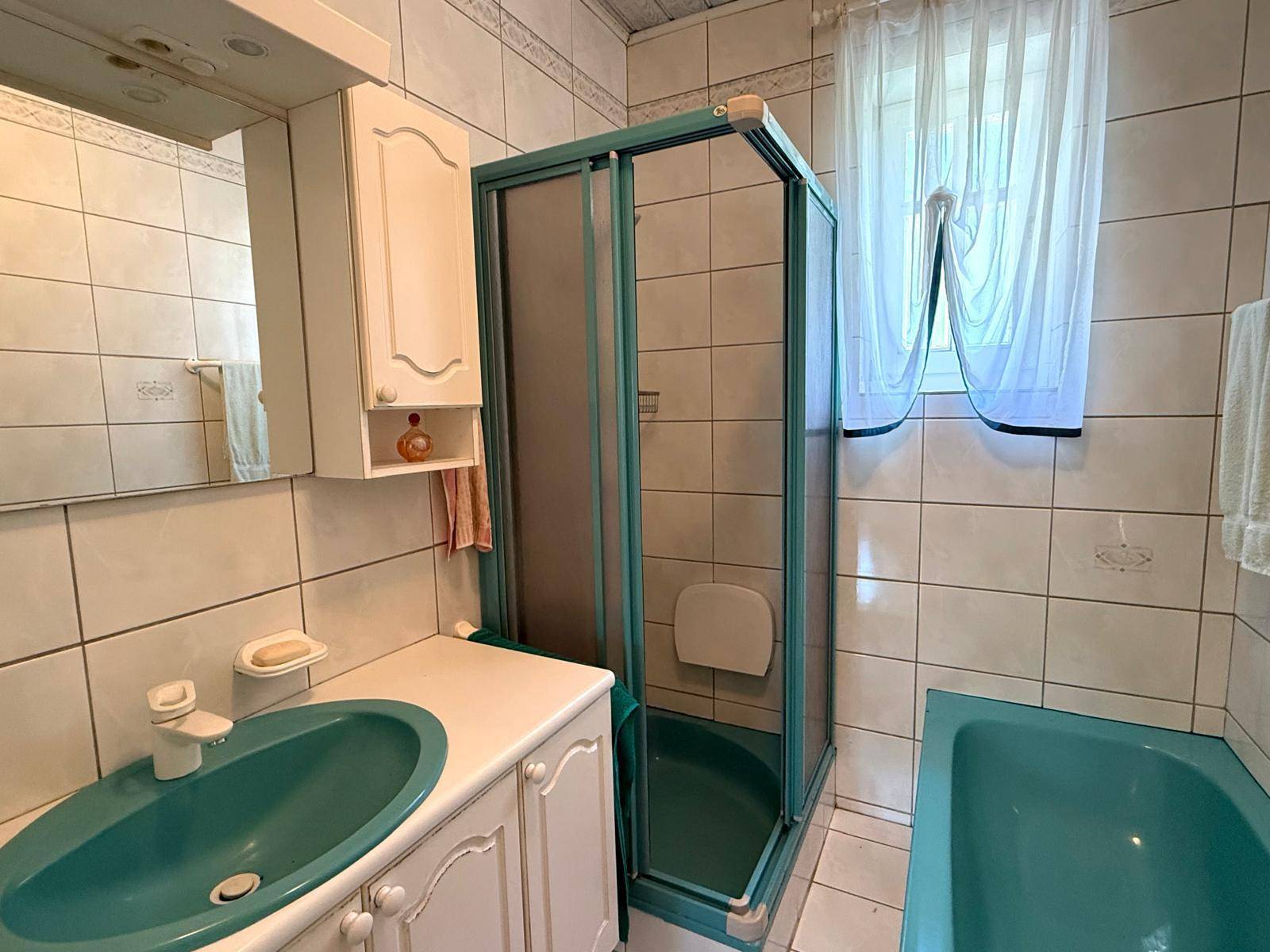 Badezimmer mit Duschkabine, türkisfarbenem Waschbecken und hellen Fliesen.