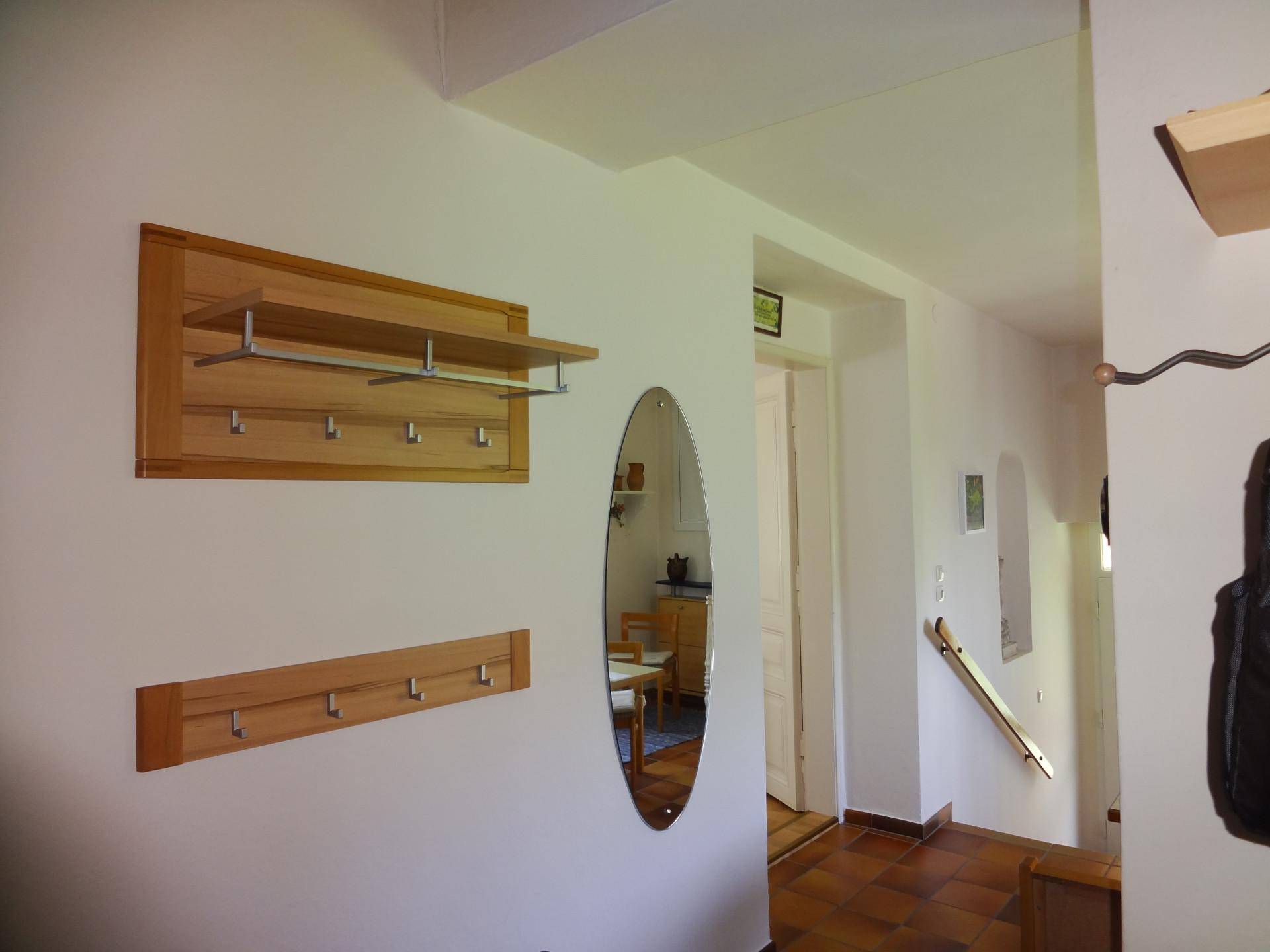 Flur mit Holzgarderobe, ovalem Spiegel und Fliesenboden.