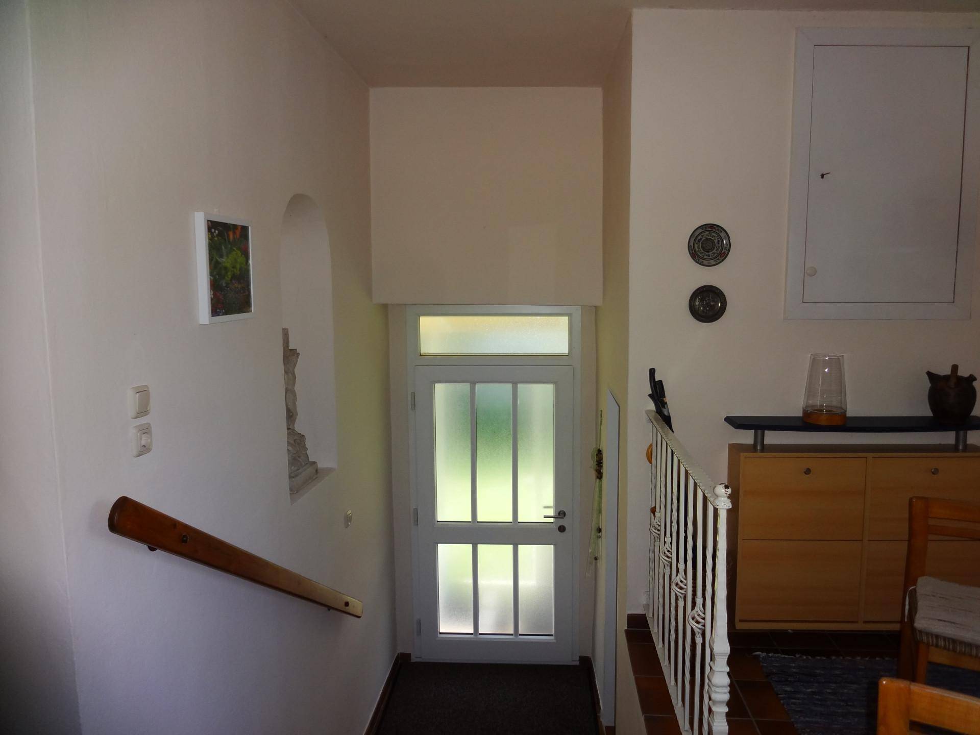 Heller Eingangsbereich mit Treppe und einer Tür mit Glaseinsätzen.