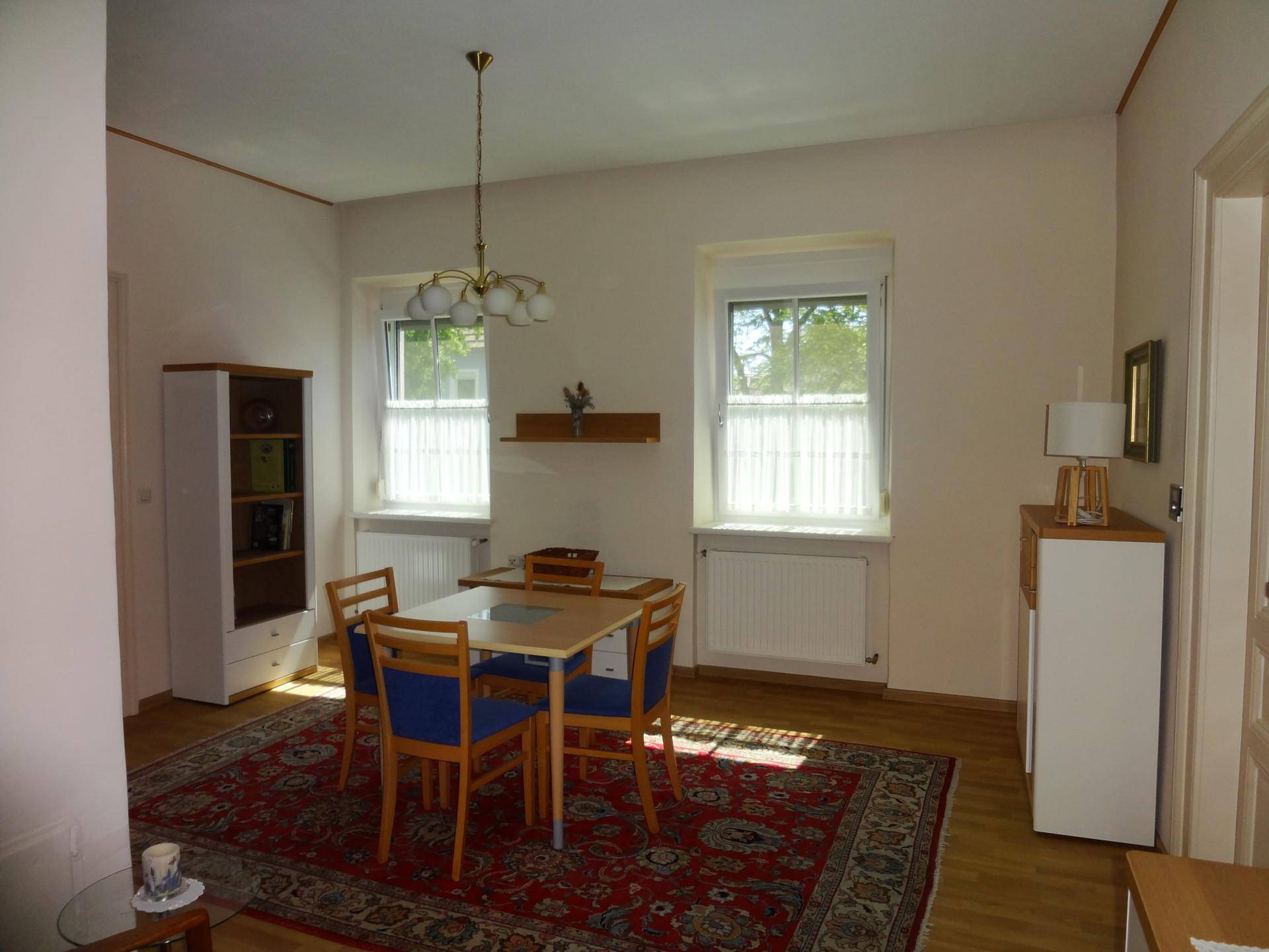 Geräumiges Esszimmer mit Holzboden, großem Teppich und viel Tageslicht.