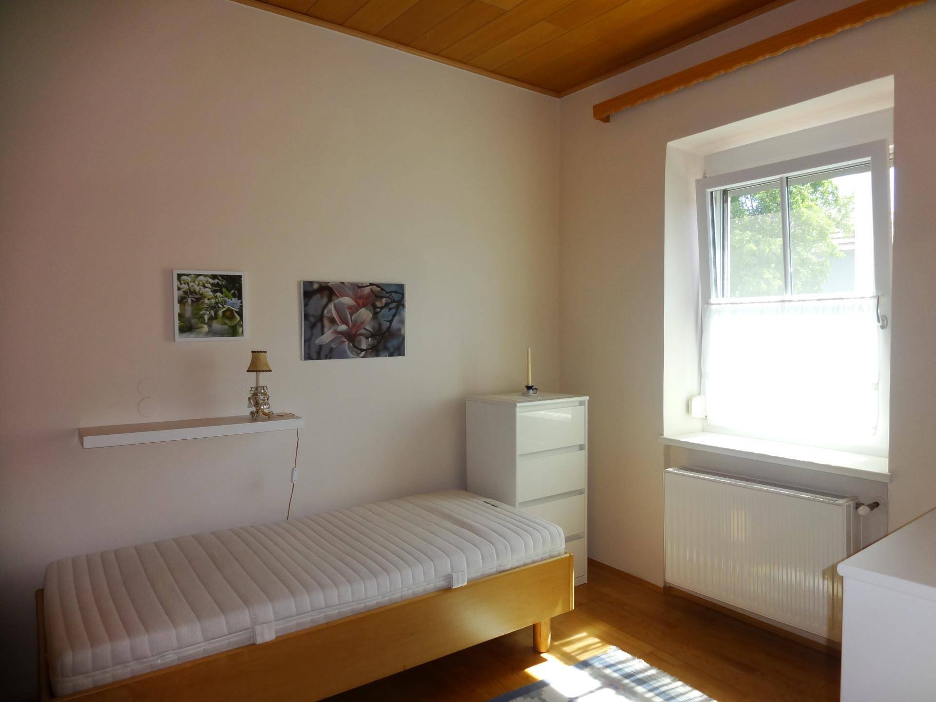Schlafzimmer mit Einzelbett, Holzboden und Holzdecke, hell durch großes Fenster.