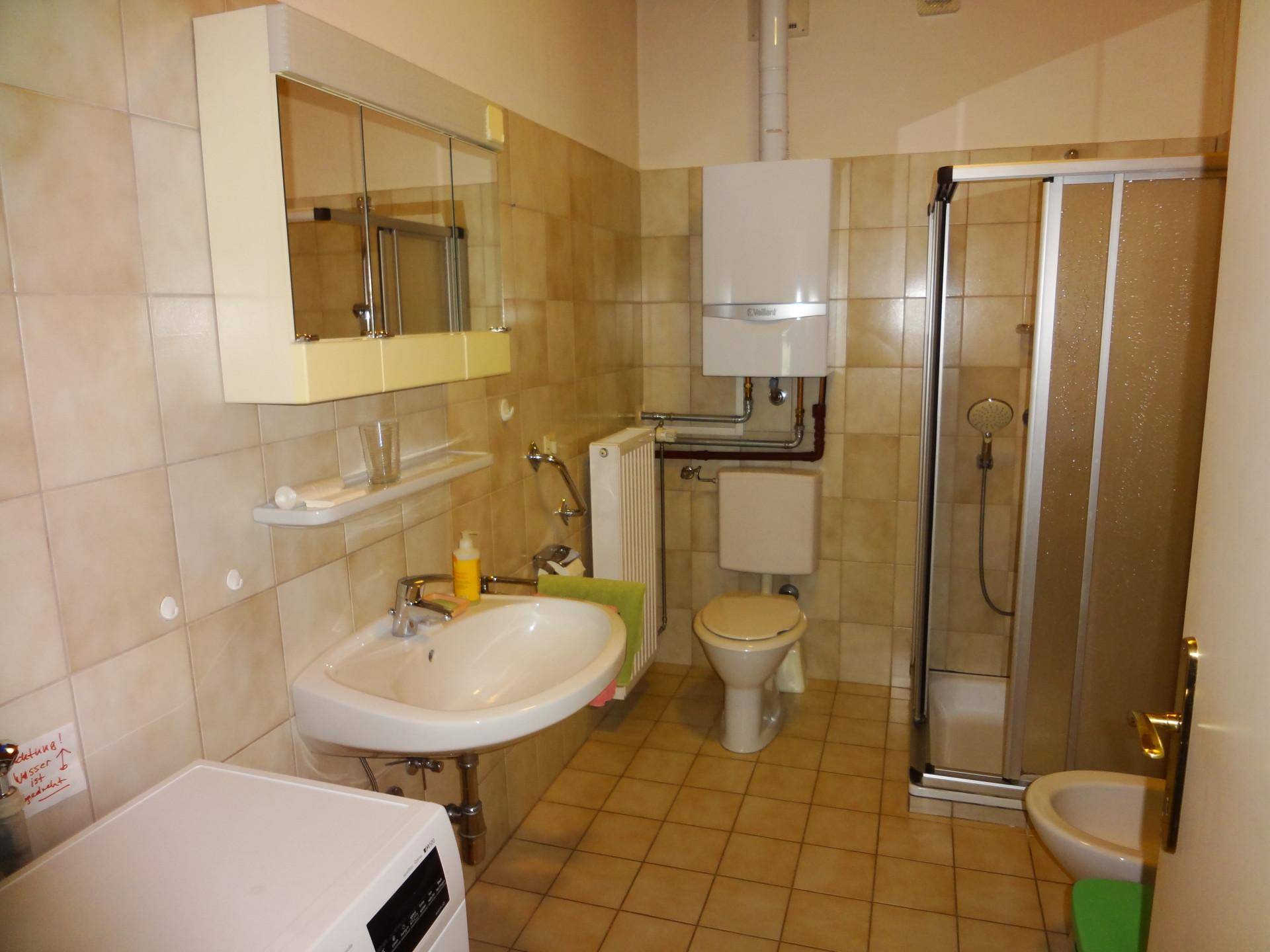 Badezimmer mit Dusche, WC, Waschbecken und Waschmaschine, komplett gefliest.