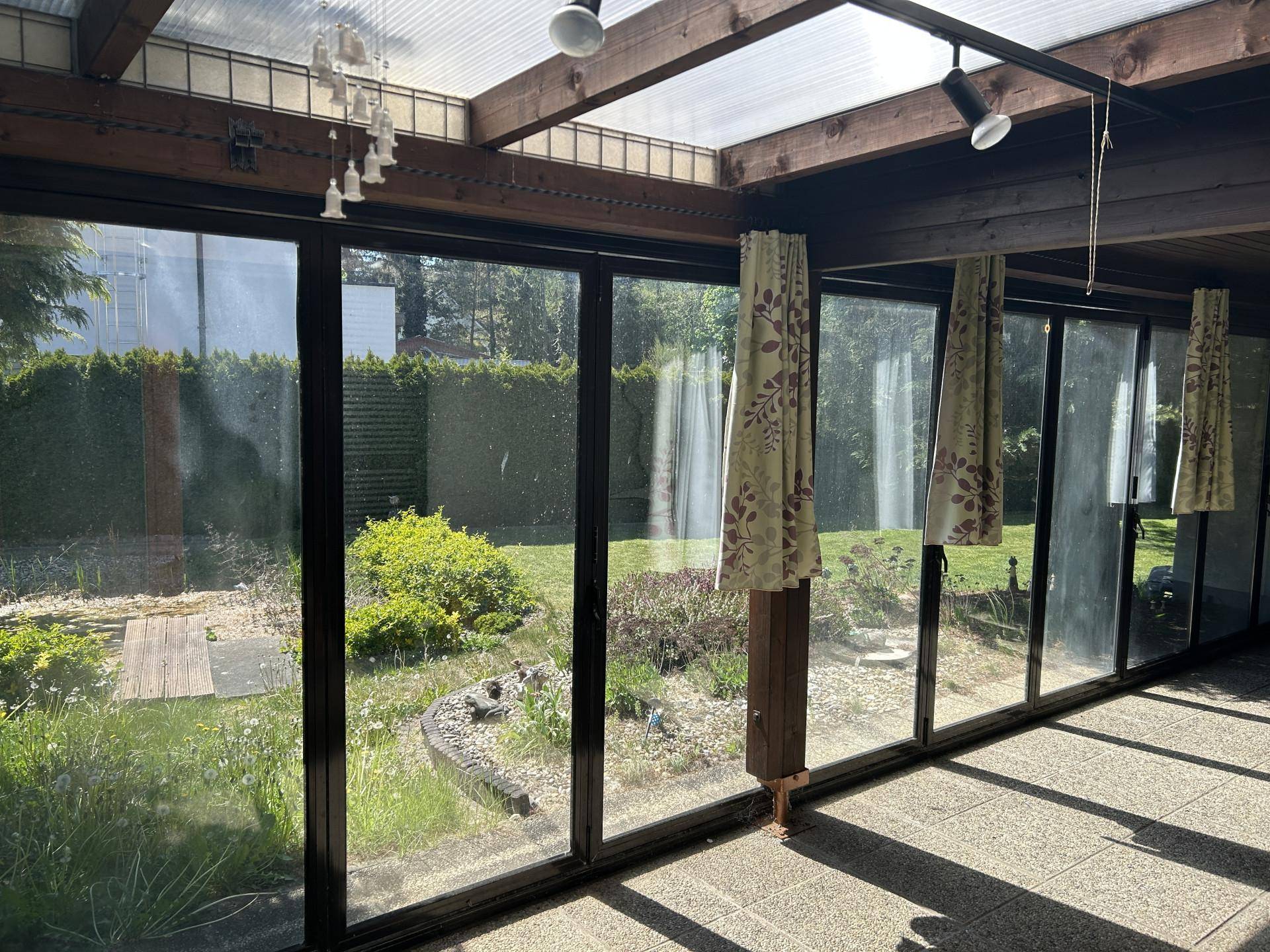 Heller Wintergarten mit großen Glasflächen, Holzbalken und direktem Blick in den grünen Garten.