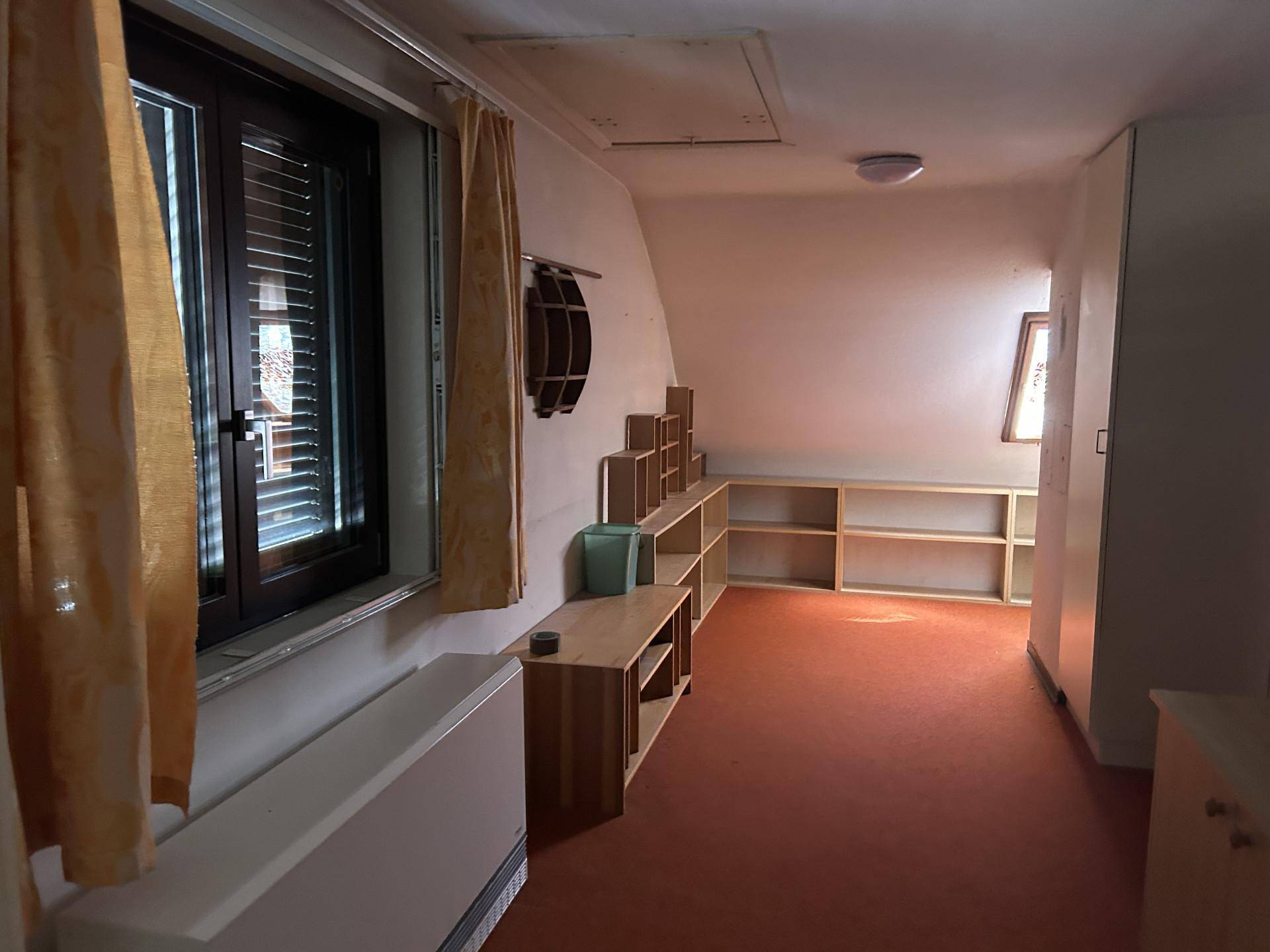 Dachzimmer mit schrägen Wänden, Fenster und eingebauten Regalen, ideal als Schlaf- oder Arbeitszimmer.