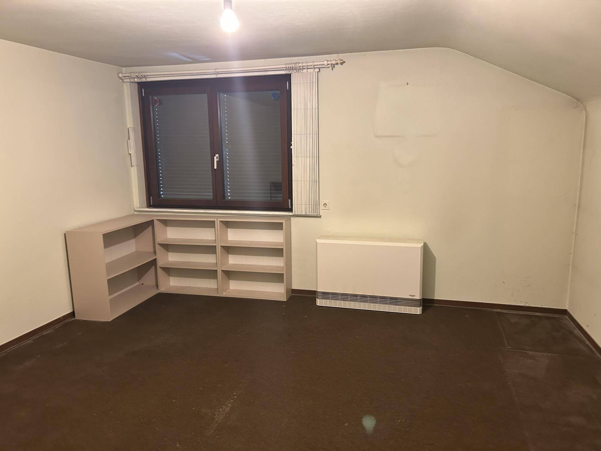 Helles Dachzimmer mit Fenster, Heizung und praktischen Regalen, bietet vielseitige Nutzungsmöglichkeiten.