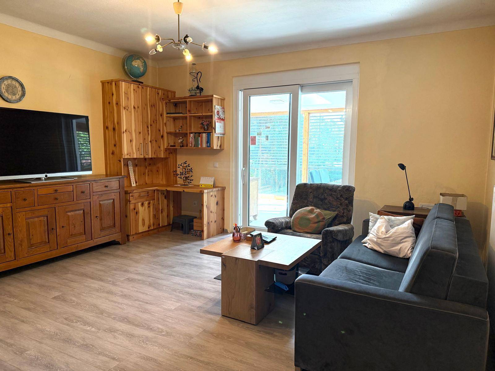 Helles Wohnzimmer mit bequemer Couch, Holzmöbeln und Zugang zu einem Wintergarten.