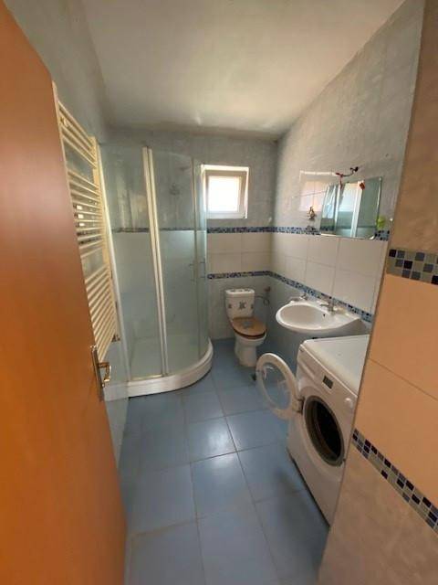Badezimmer mit blauen Fliesen, Duschkabine, WC, Waschbecken und Waschmaschine.