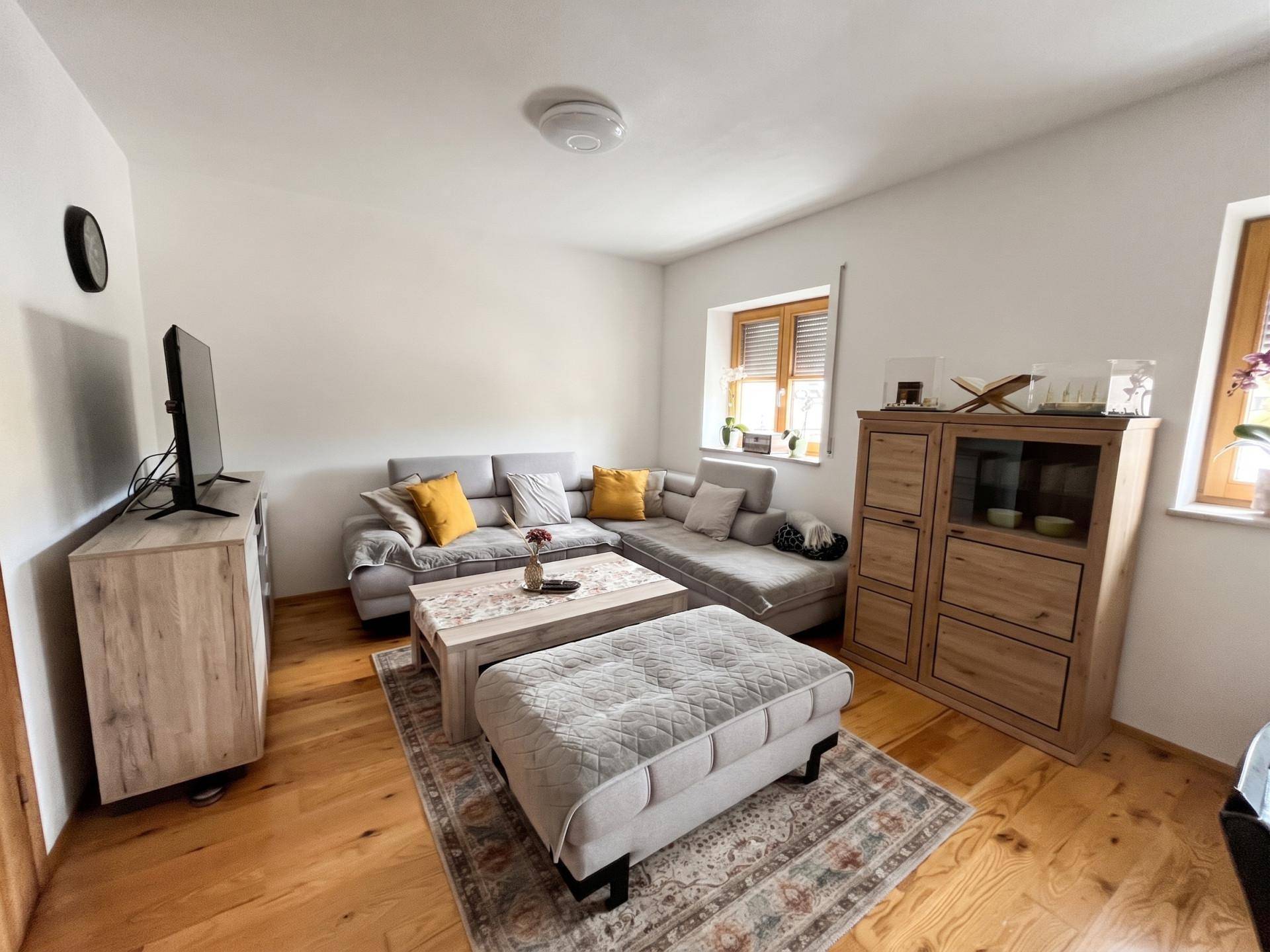 Helles Wohnzimmer mit Ecksofa, Couchtisch und Holzmöbeln auf Parkettboden.