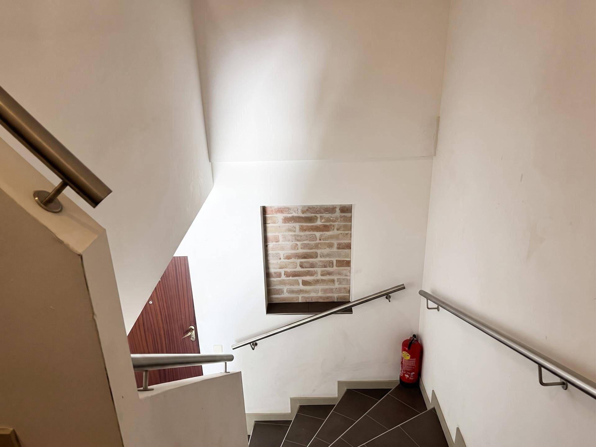 Treppenhaus mit Fliesenboden, Edelstahlgeländer und Ziegelwandakzent.