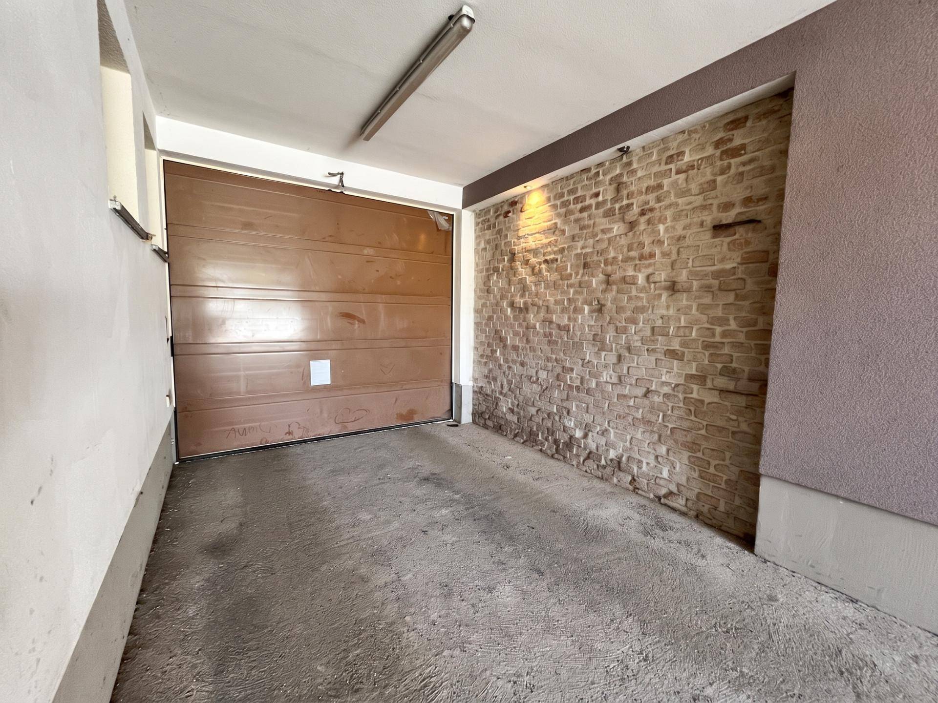 Leere Garage mit Rolltor, Ziegelwand und Betonboden, bereit zur Nutzung.