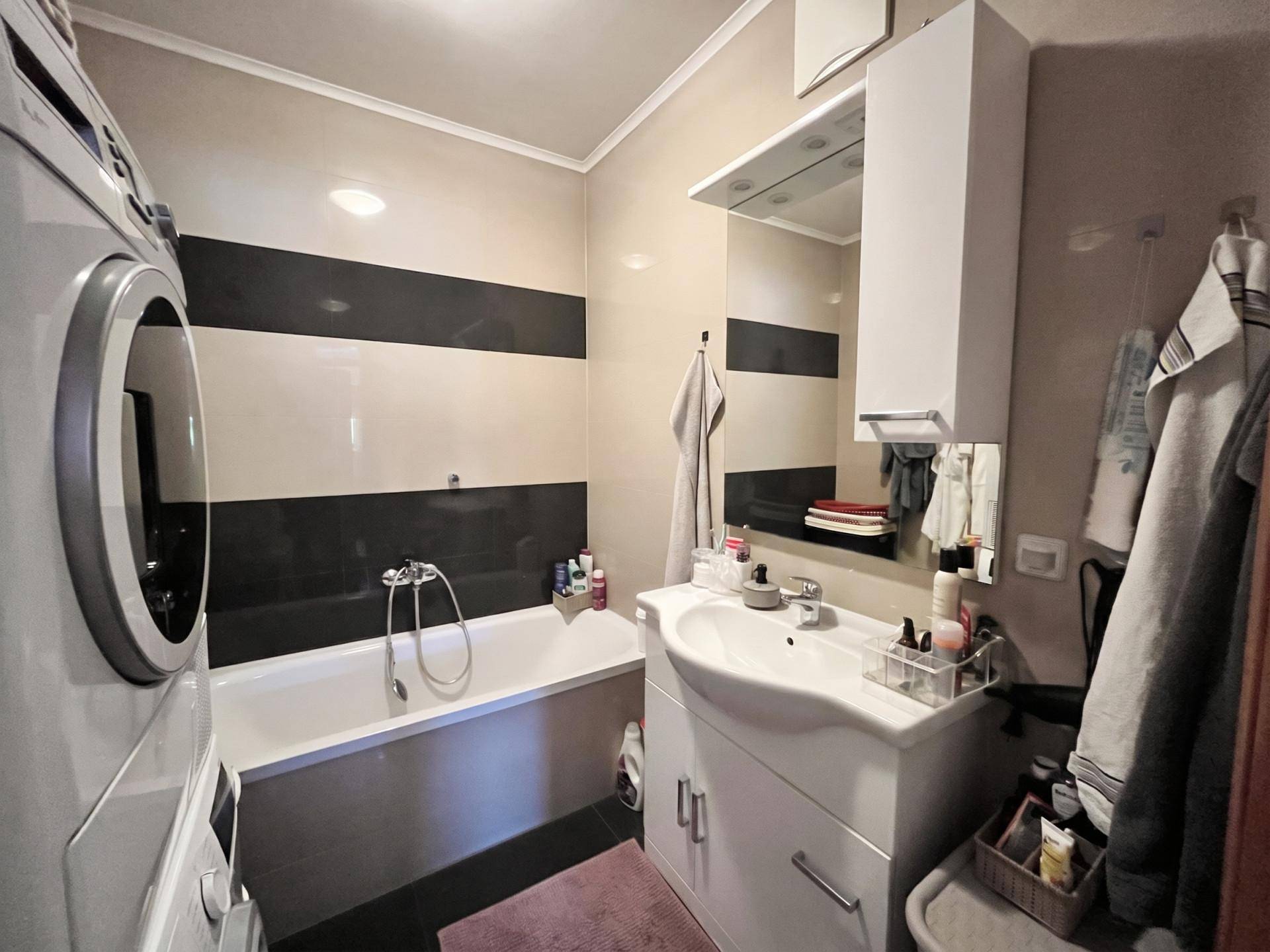 Badezimmer mit Badewanne, Waschbecken und Waschmaschine, ausgestattet mit modernen Fliesen in Schwarz und Beige.