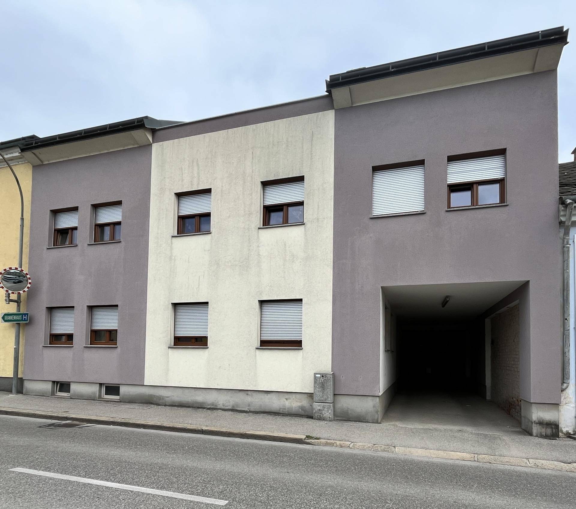 Mehrfamilienhaus mit moderner Fassade in Grau und Beige, mit Rollläden an den Fenstern.