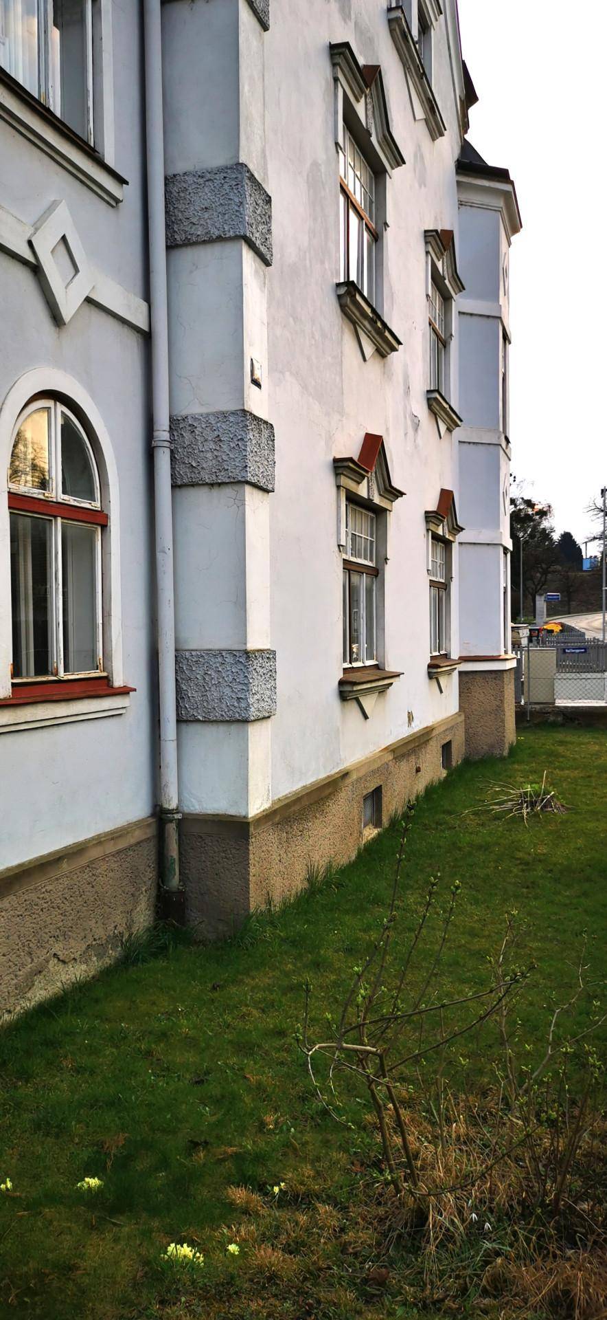 Seitenansicht des Gebäudes mit Details der Fassade, Fenstern und einem schmalen Rasenstreifen.