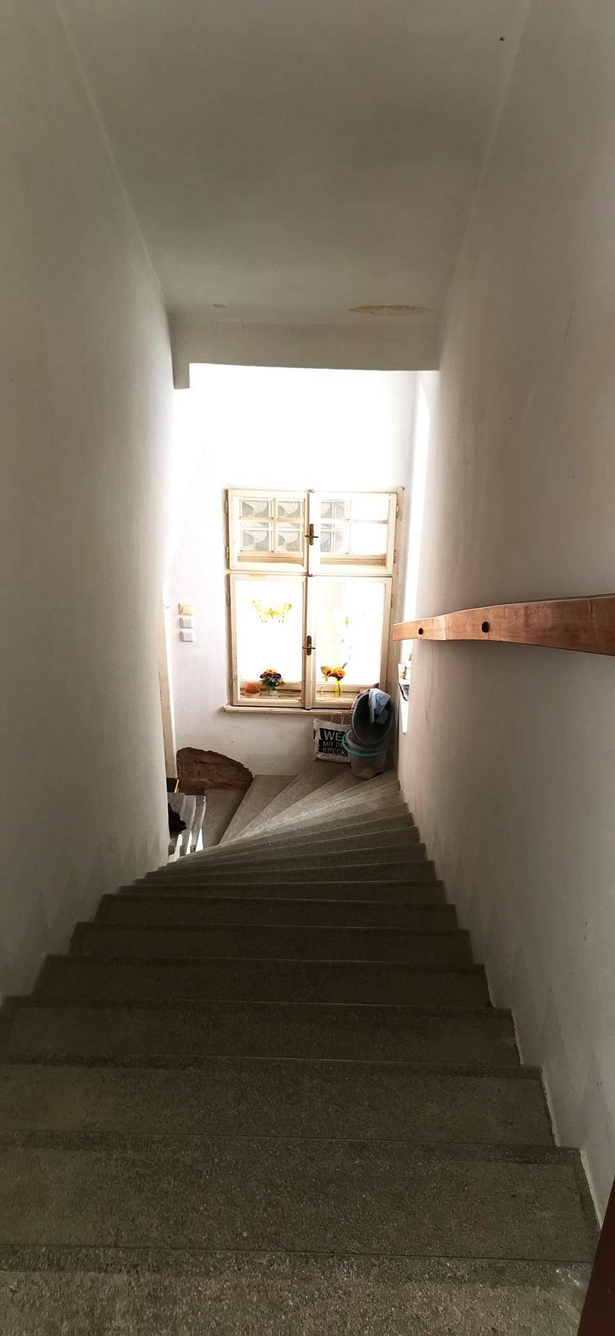 Treppenhaus mit Steinstufen und einem Fenster am Treppenabsatz, das Tageslicht hereinlässt.