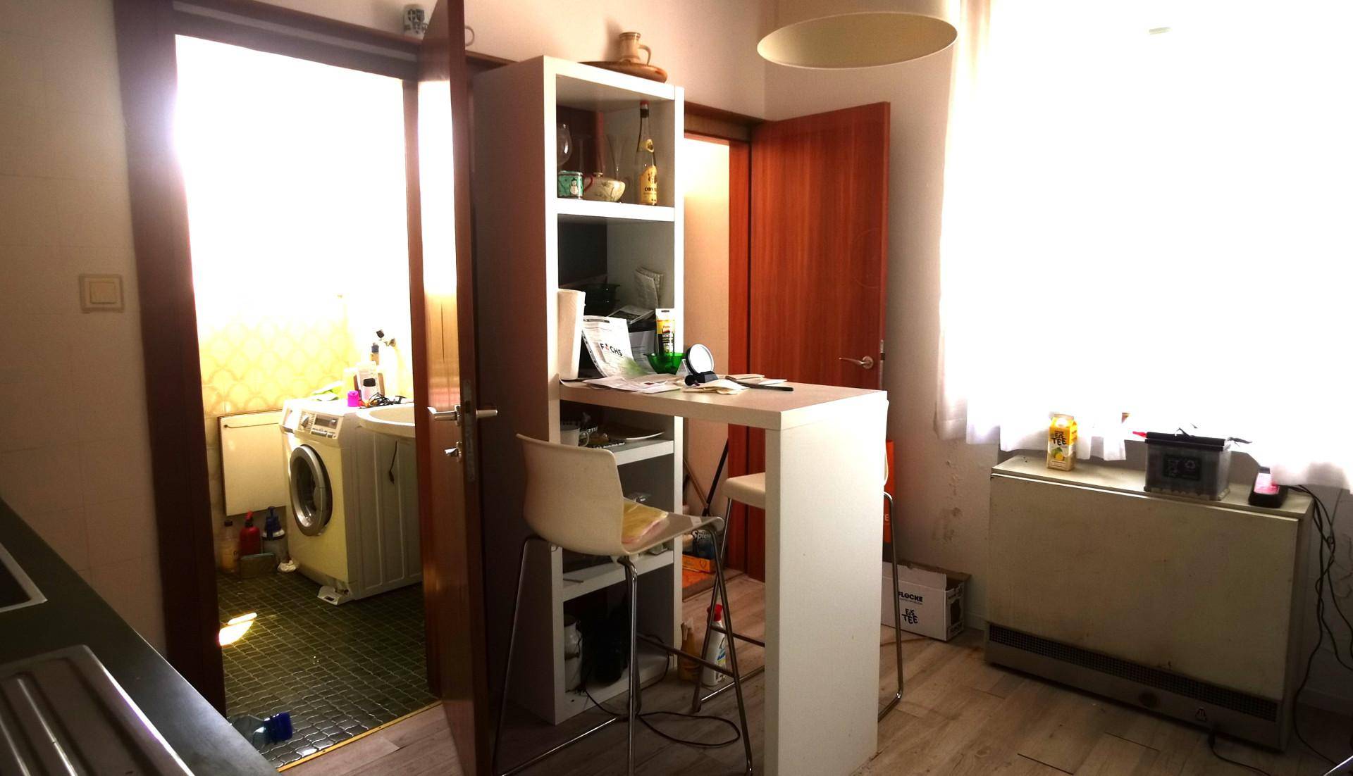 Kleine Küche mit Frühstücksbar und Blick auf einen angrenzenden Waschraum mit Waschmaschine.