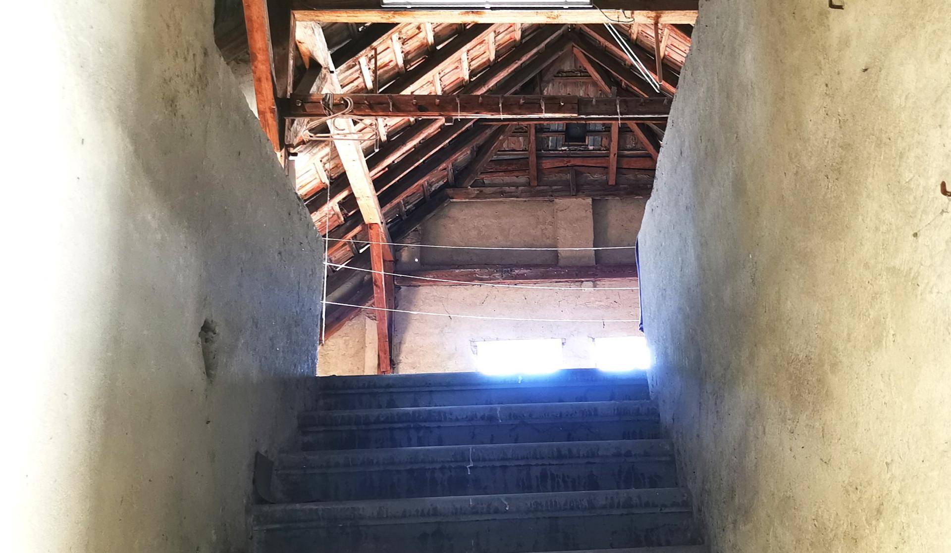 Treppenaufgang führt zu einem unfertigen Dachboden mit sichtbarer Holzkonstruktion und Dachschrägen.