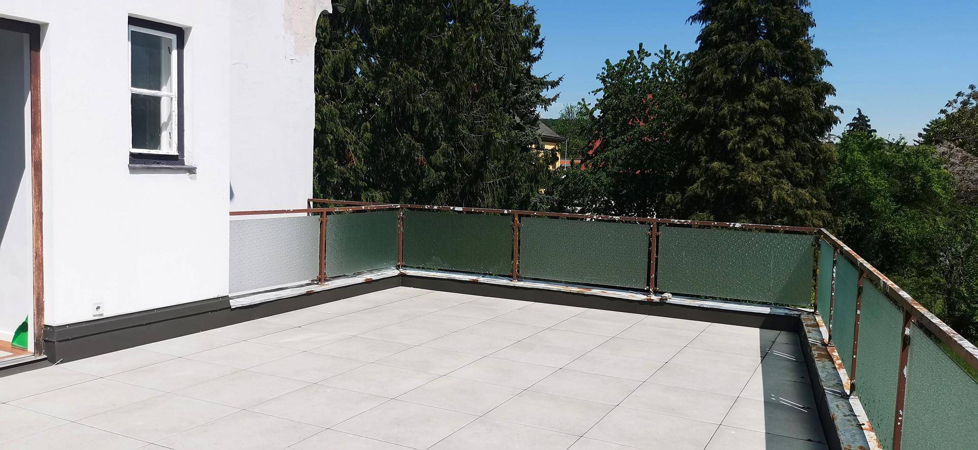 Geräumige geflieste Terrasse mit Glasgeländer und Blick ins Grüne, ideal für Entspannung im Freien.
