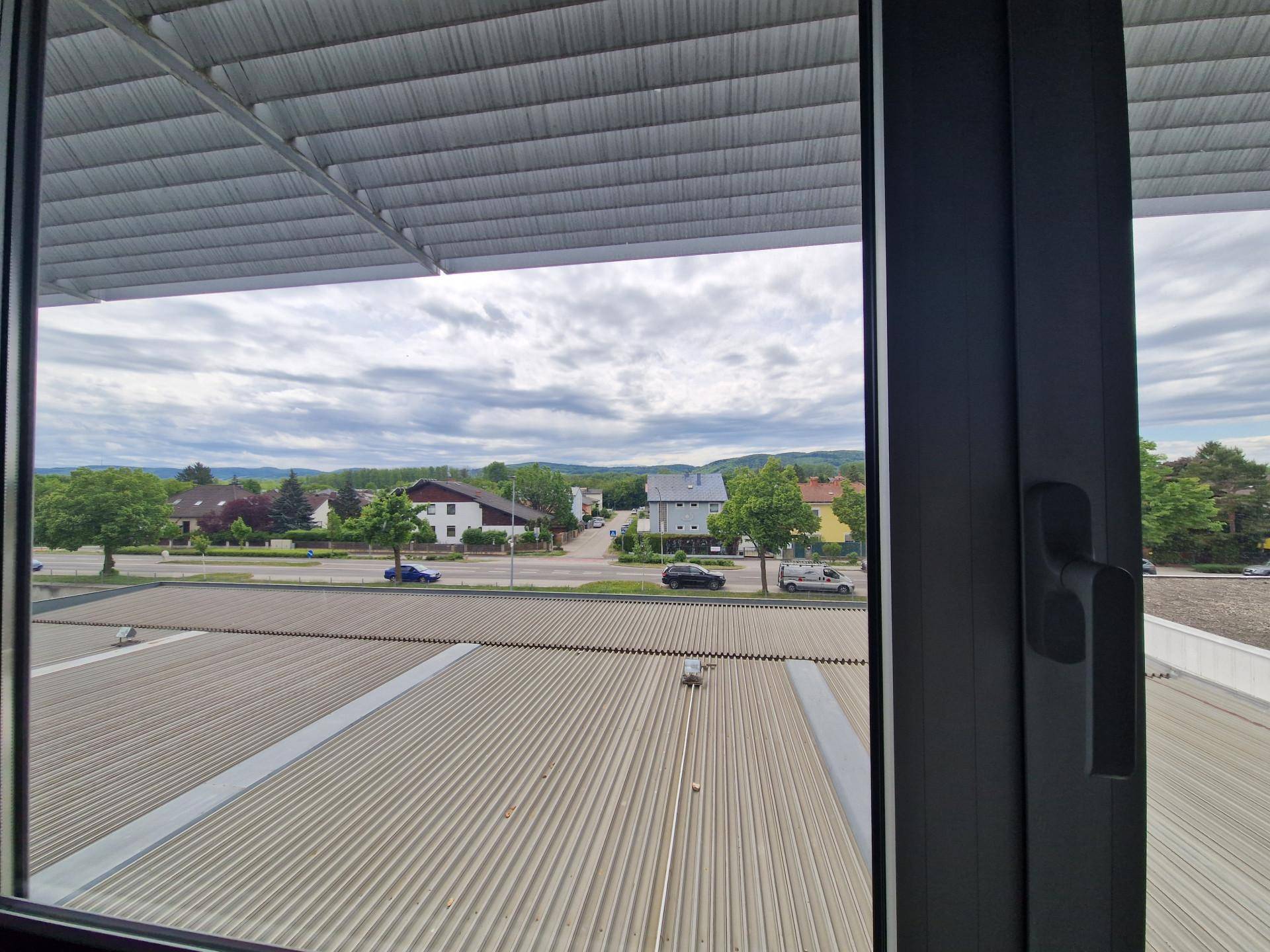 Ausblick aus einem Fenster auf eine Straße, Häuser und grüne Landschaft.
