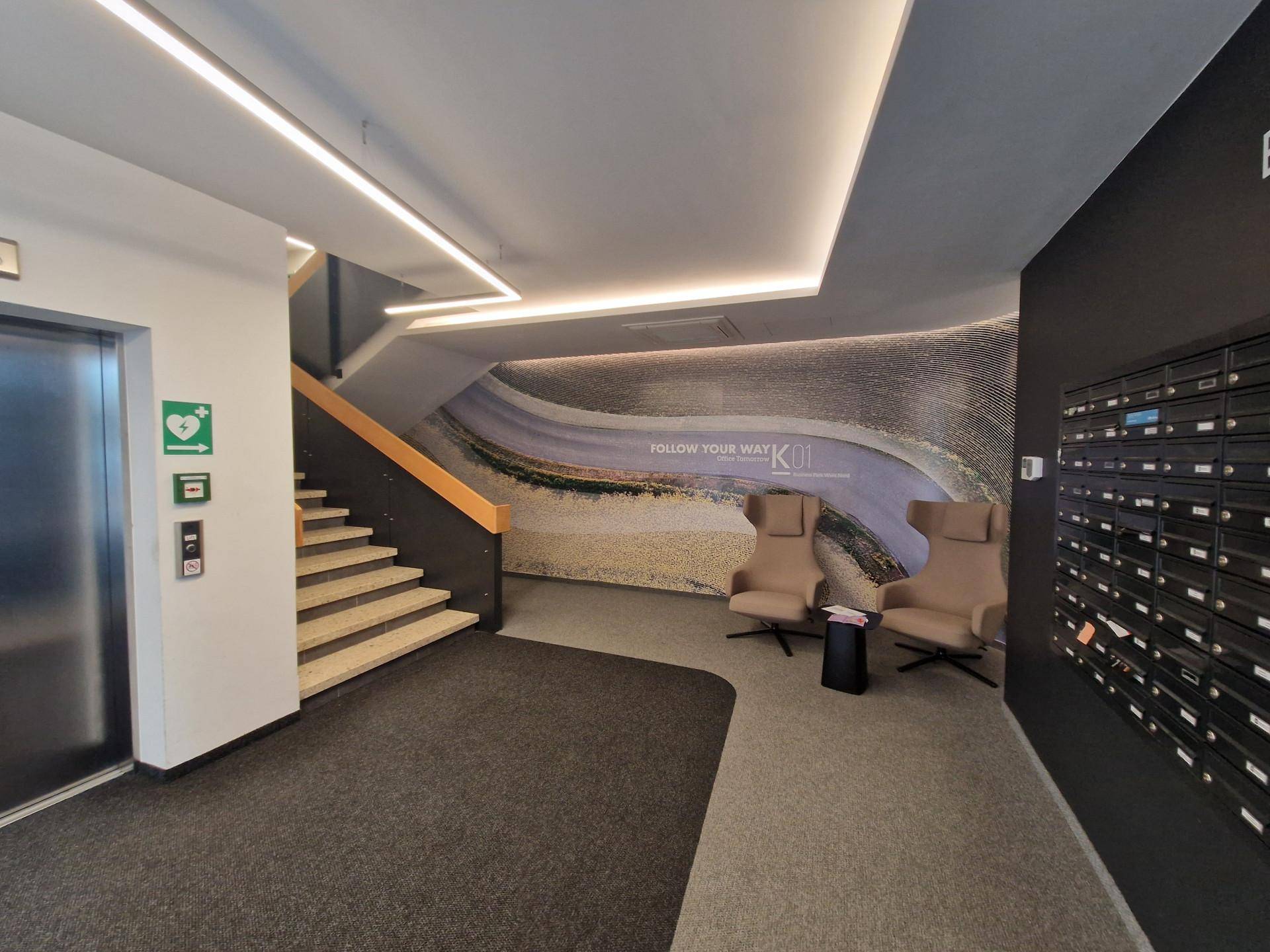 Modern gestalteter Eingangsbereich mit Aufzug, Treppe, Briefkästen und Sitzgelegenheiten in einem Geschäftsgebäude.