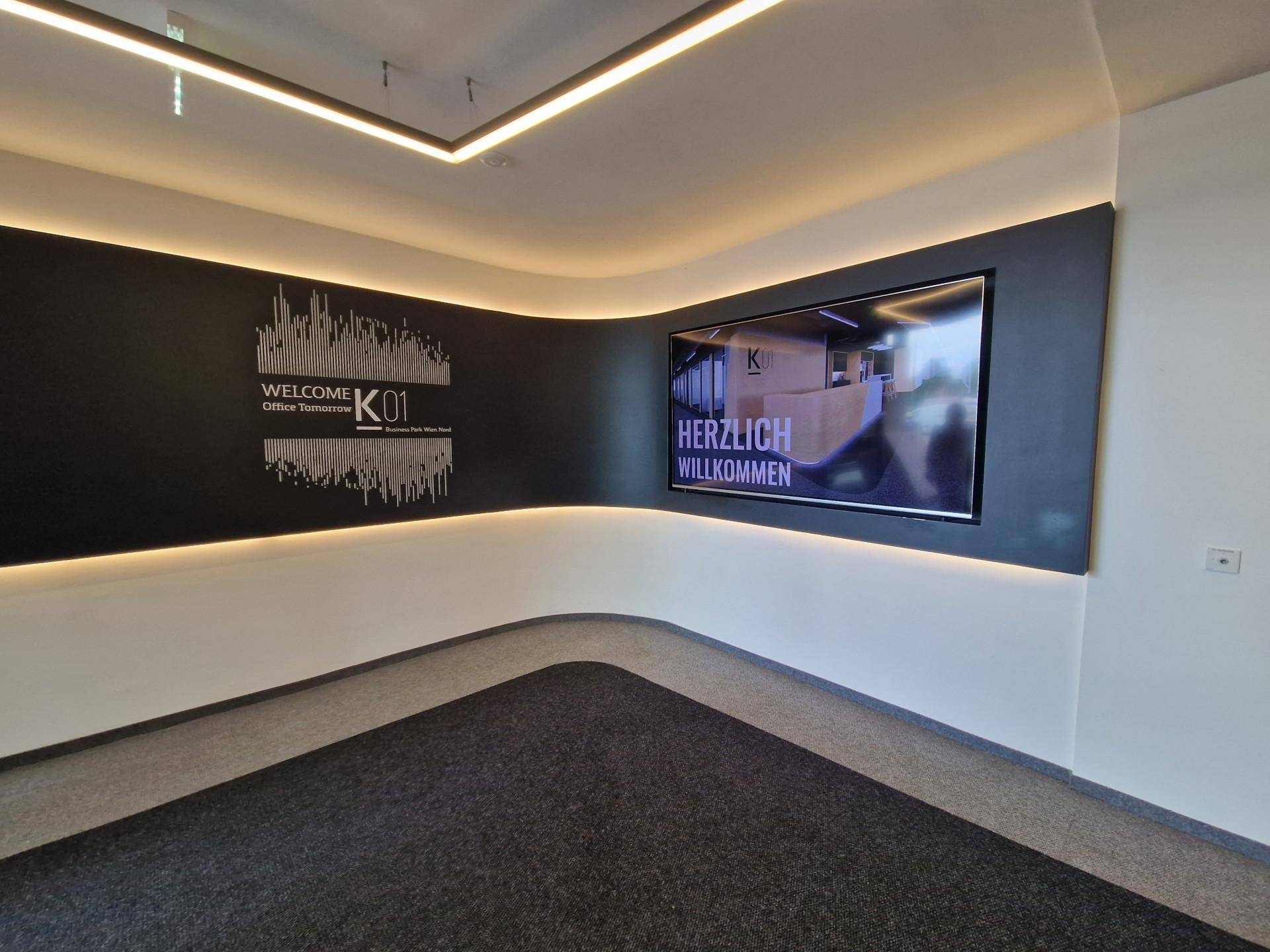 Moderner Empfangsbereich mit großem Bildschirm und indirekter Beleuchtung an der Wand in einem Geschäftsgebäude.
